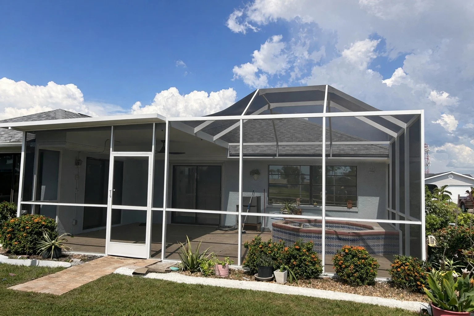 A house with a screened porch, a hot tub, and potted plants under a partly cloudy sky.