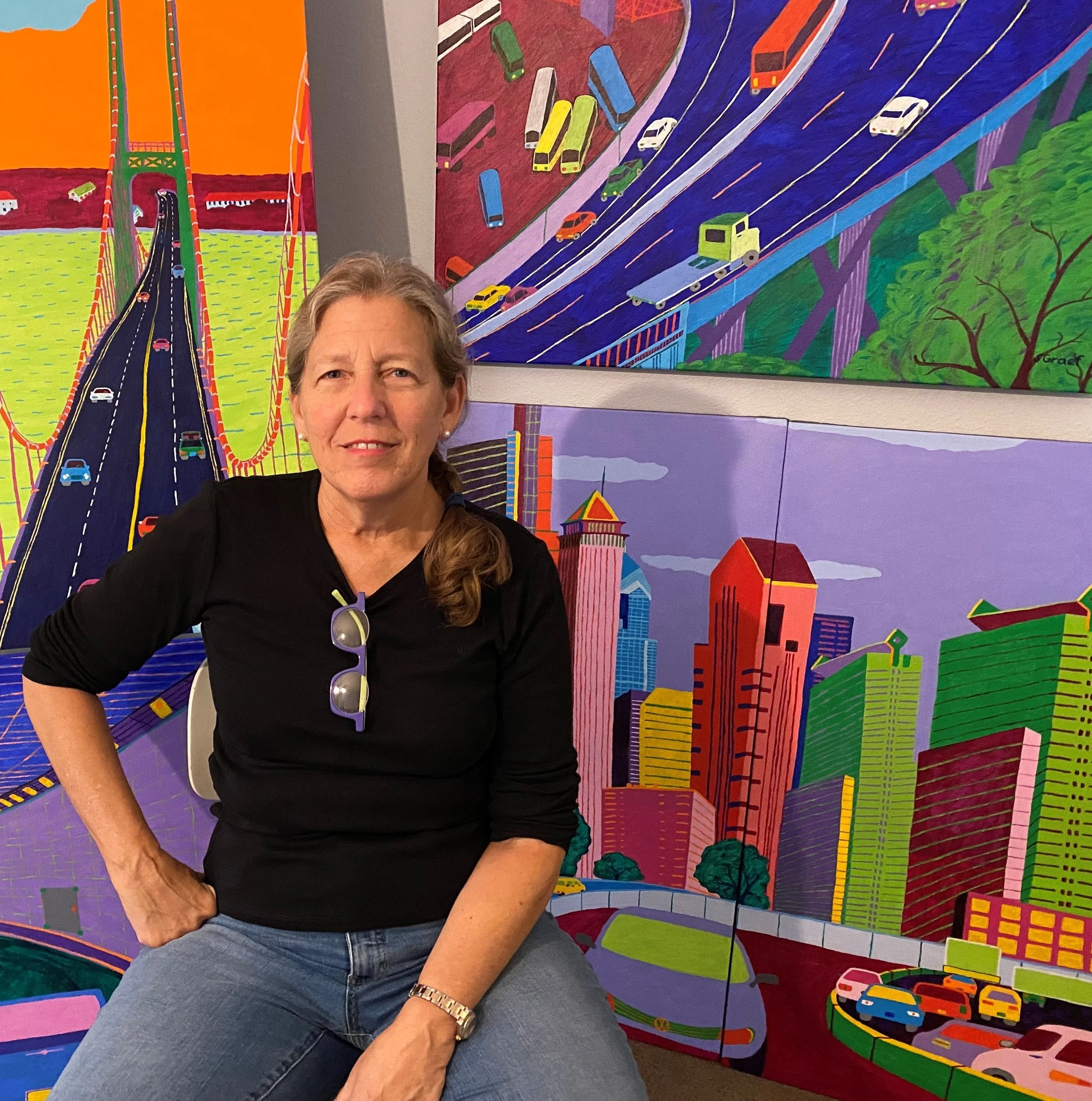 Sue Graef, Juror's Choice Best in Show winner for CEV Art Gallery's Chromatic exhibition, seated in front of her colorful skyline paintings