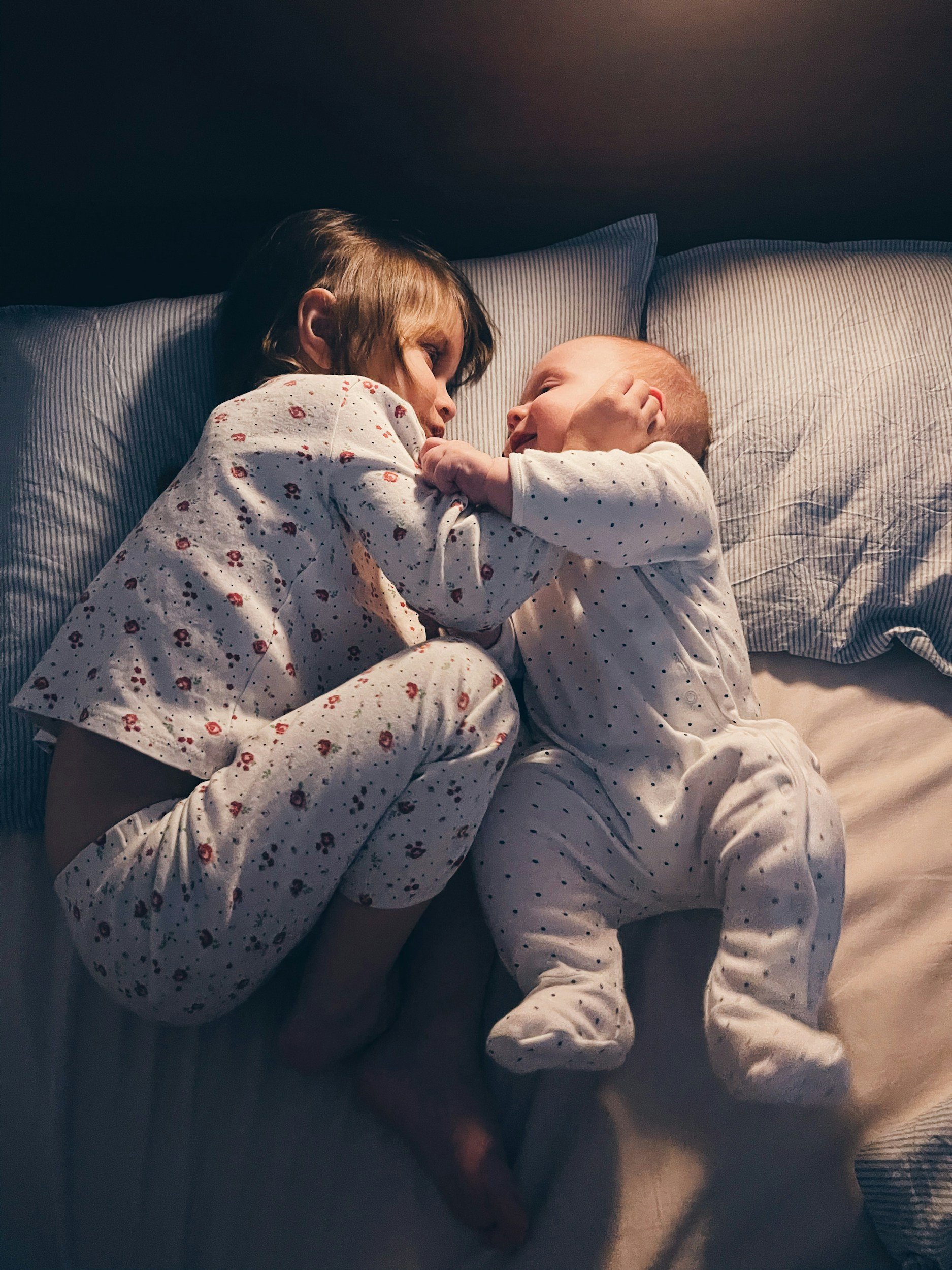Baby and toddler snuggling in bed together smiling