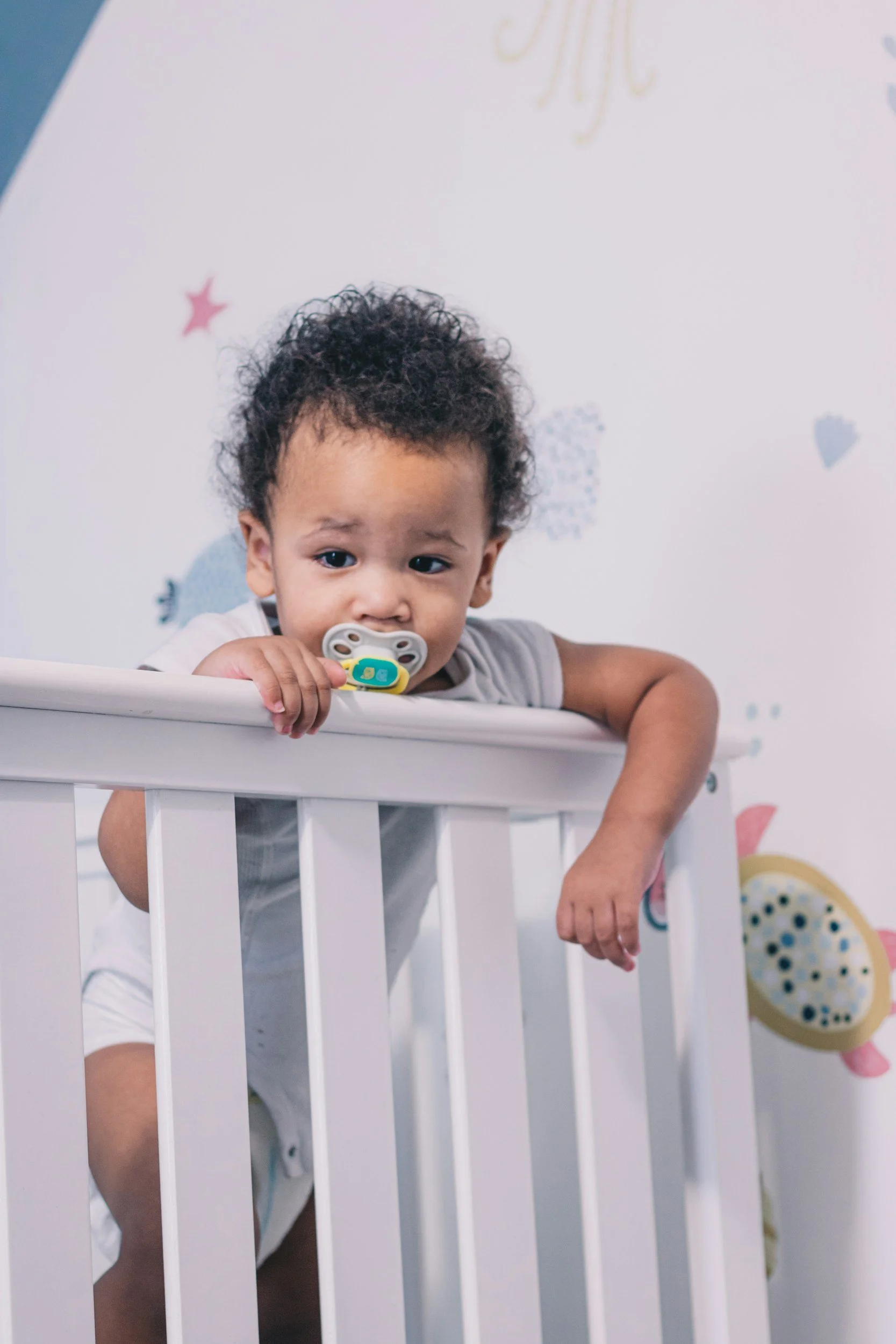 Infant standing in a crib with a pacifier