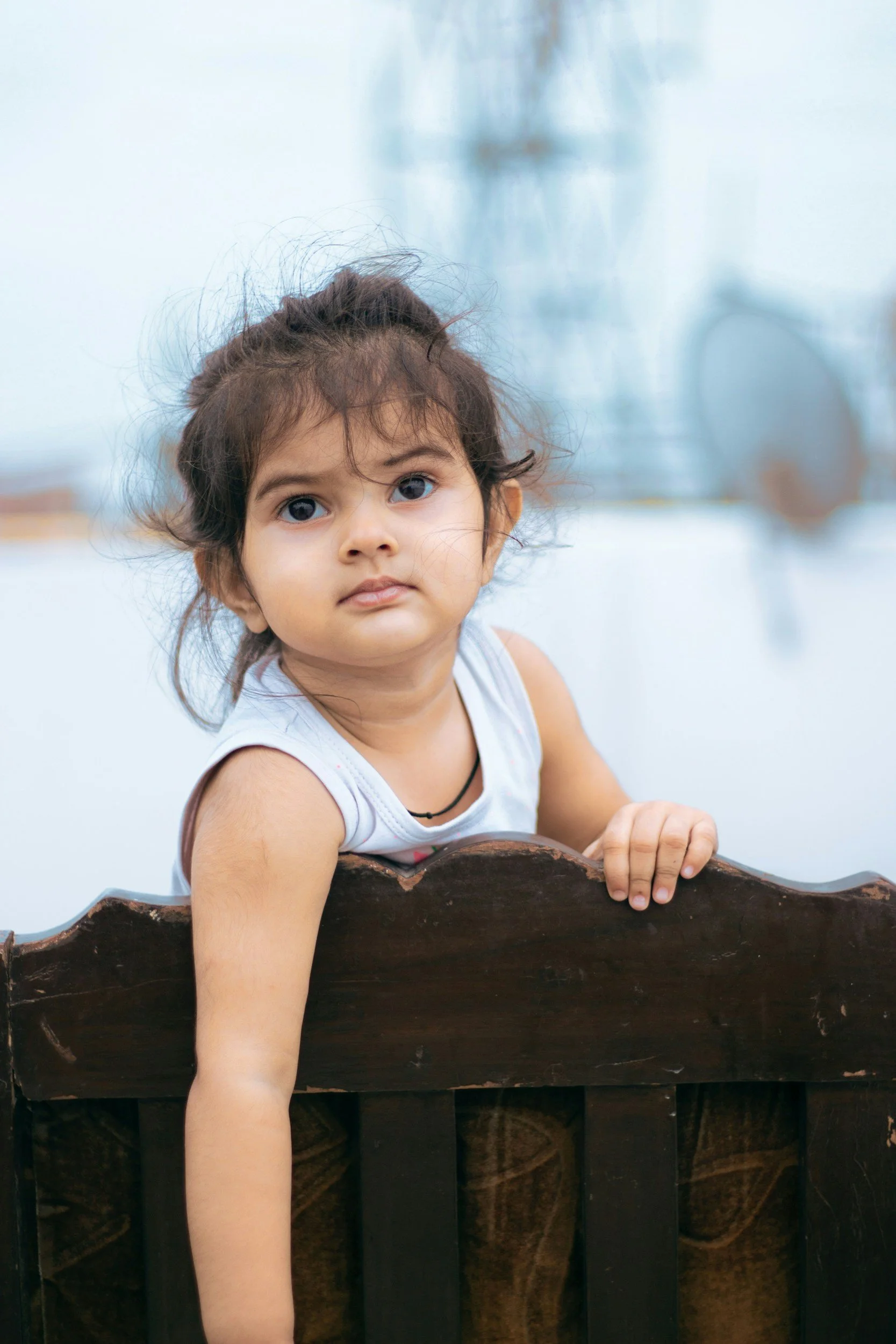 Toddler holding onto a wooden crib rail and looking toward the camera
