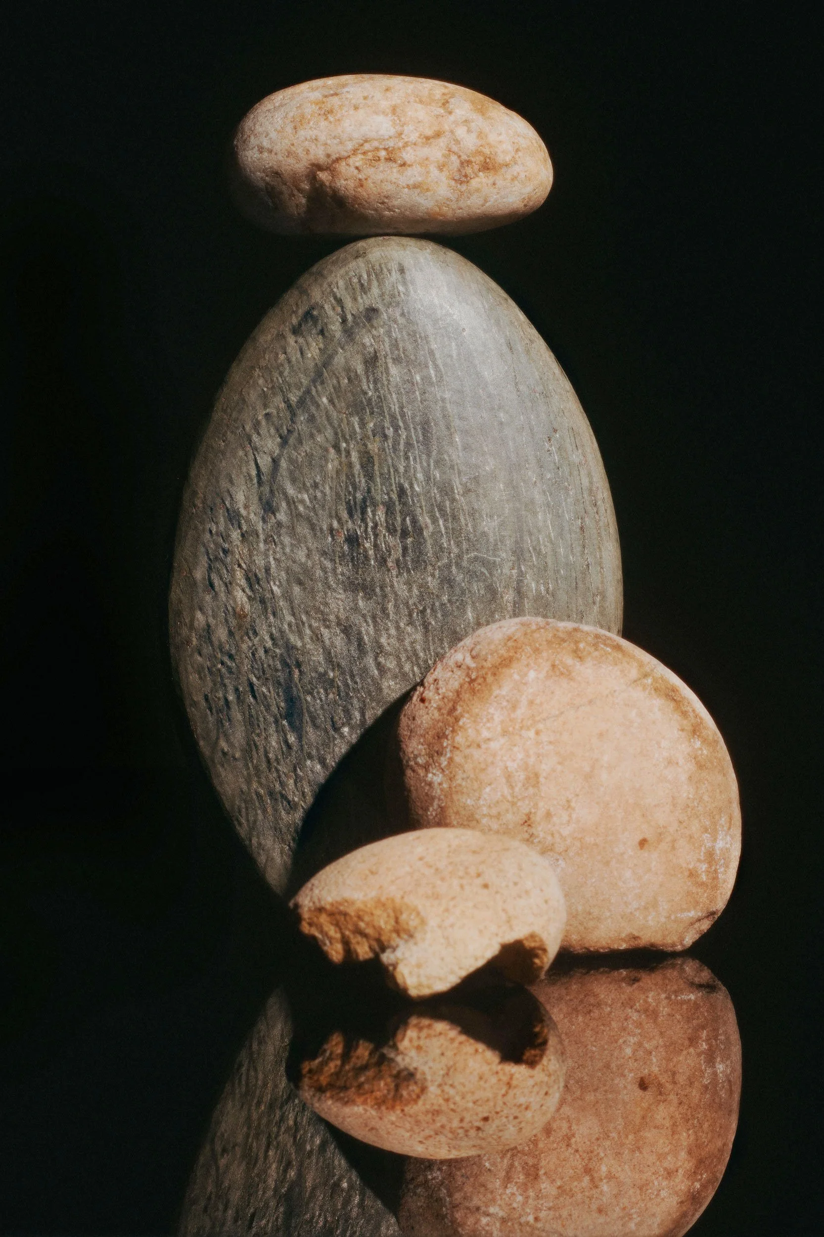 Five different-sized smooth rocks stacked vertically with a dark background and their reflection on a glossy surface.