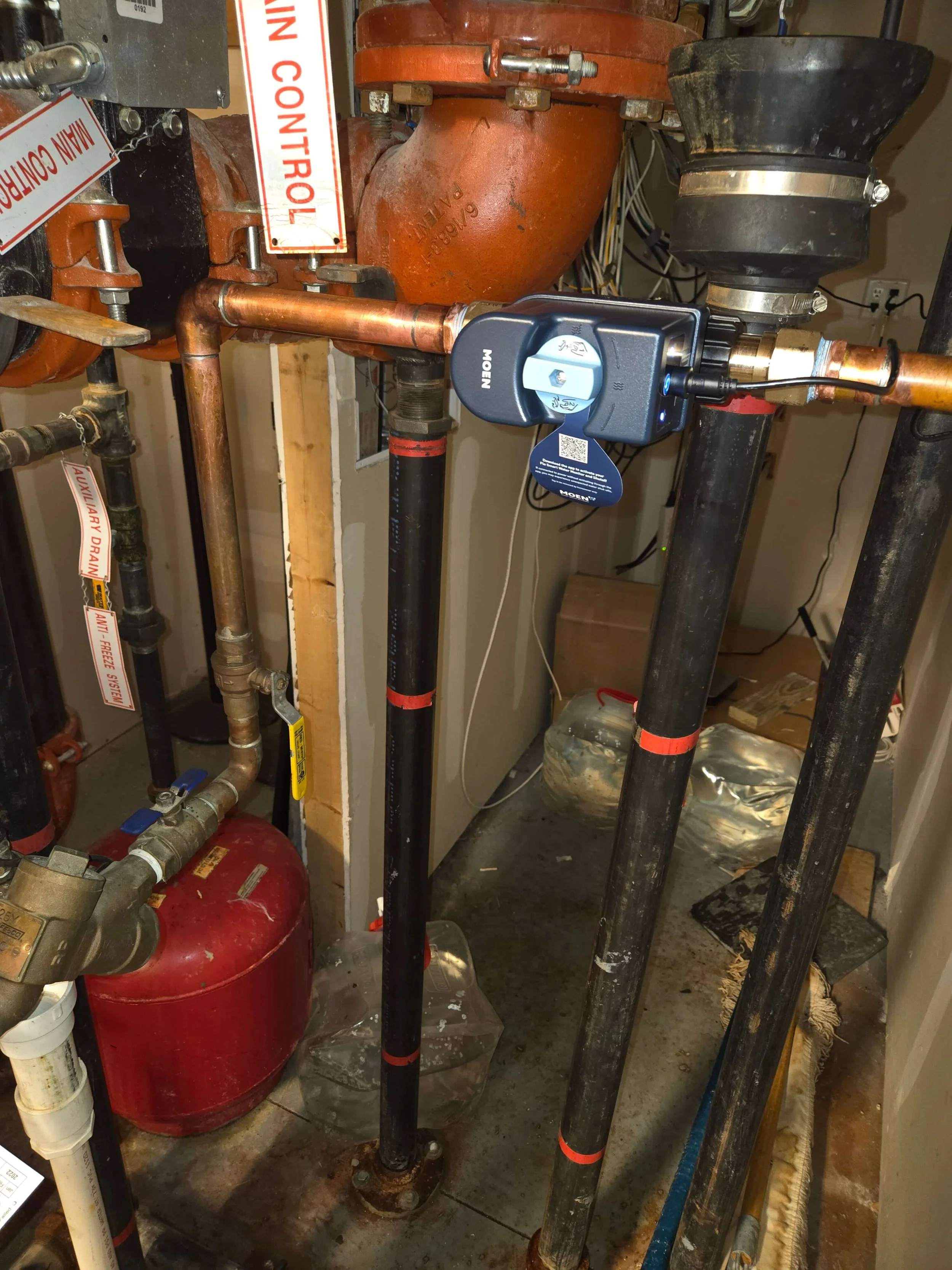 A plumbing system featuring black pipes, copper pipes, a red expansion tank, and a digital control device attached to the copper piping.