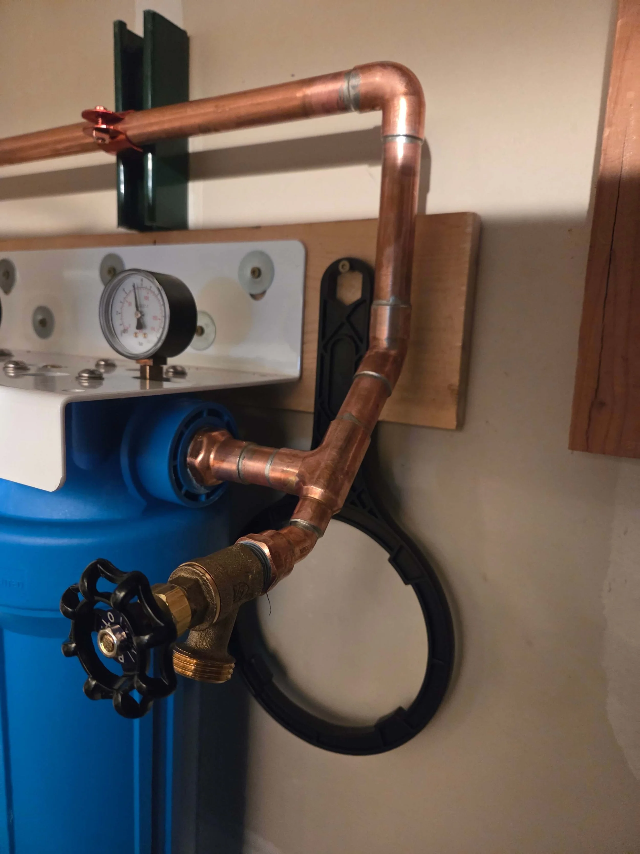 Close-up of copper piping connected to a water filtration system with a black valve handle and a pressure gauge.