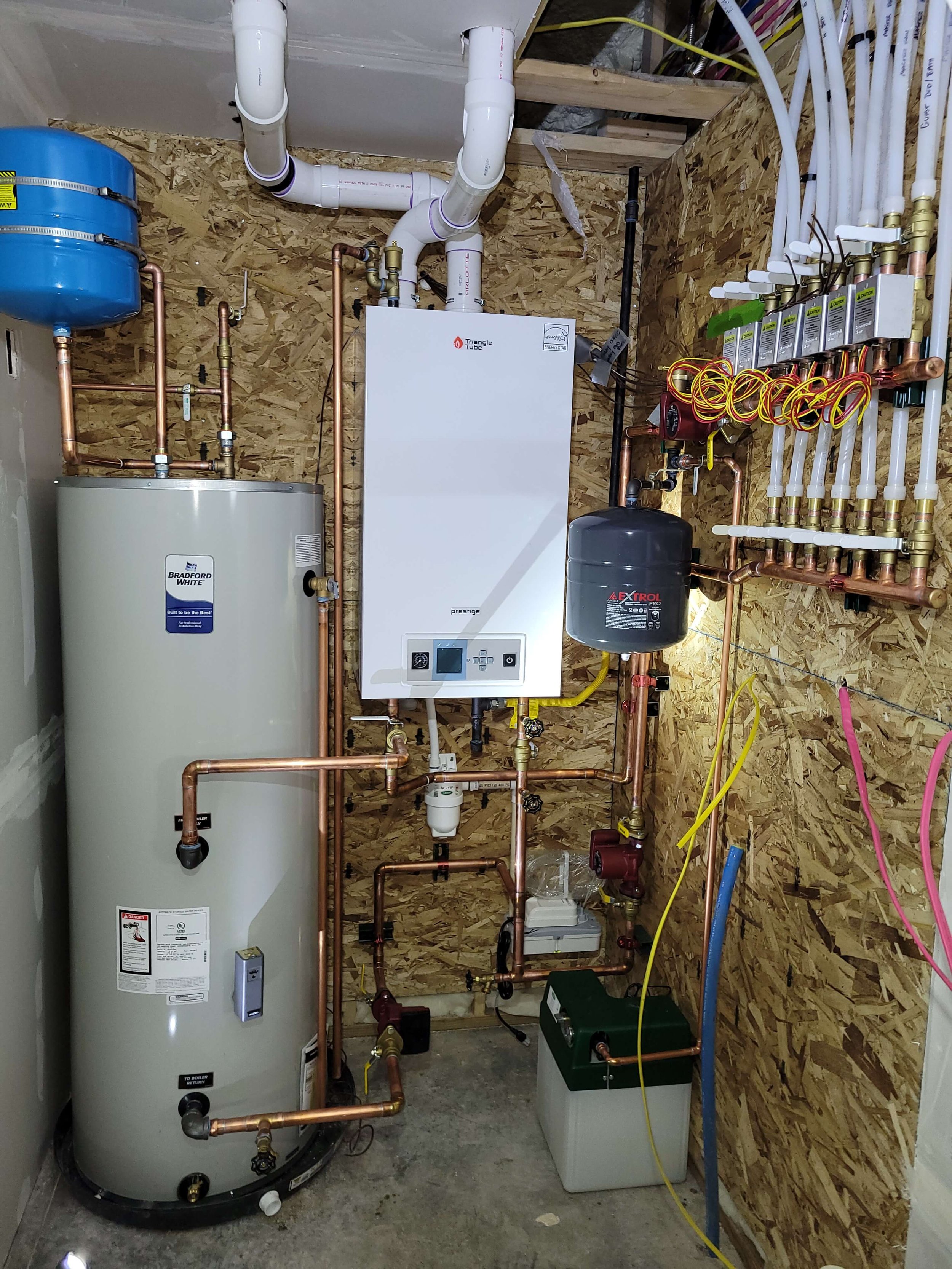 Boiler room setup with water heater, pipes, pressure tank on wall, control panel, and various plumbing connections made of copper and PVC.