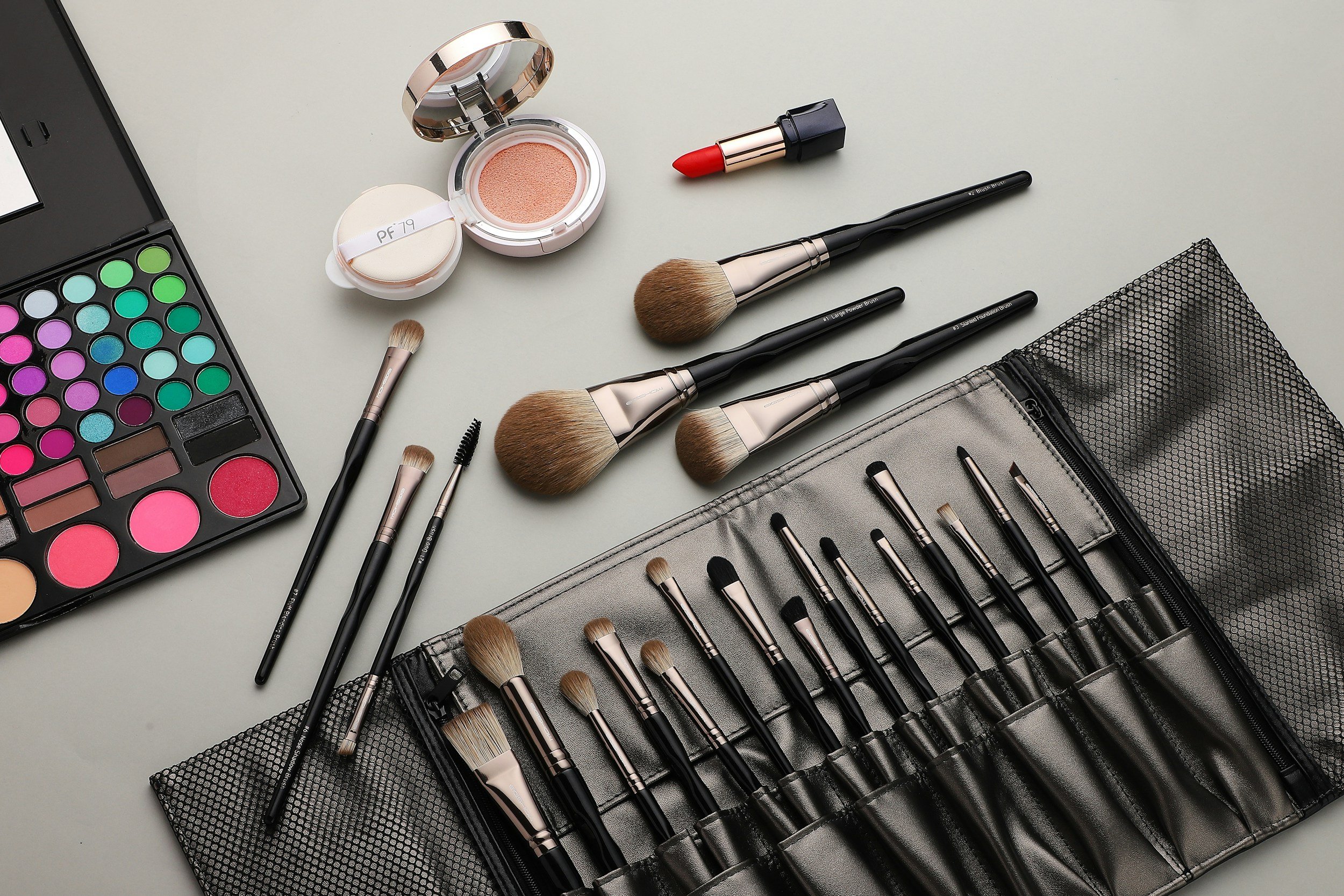 A collection of makeup tools including brushes, eyeshadow palette, blush, lipstick, and makeup bag on a white surface.