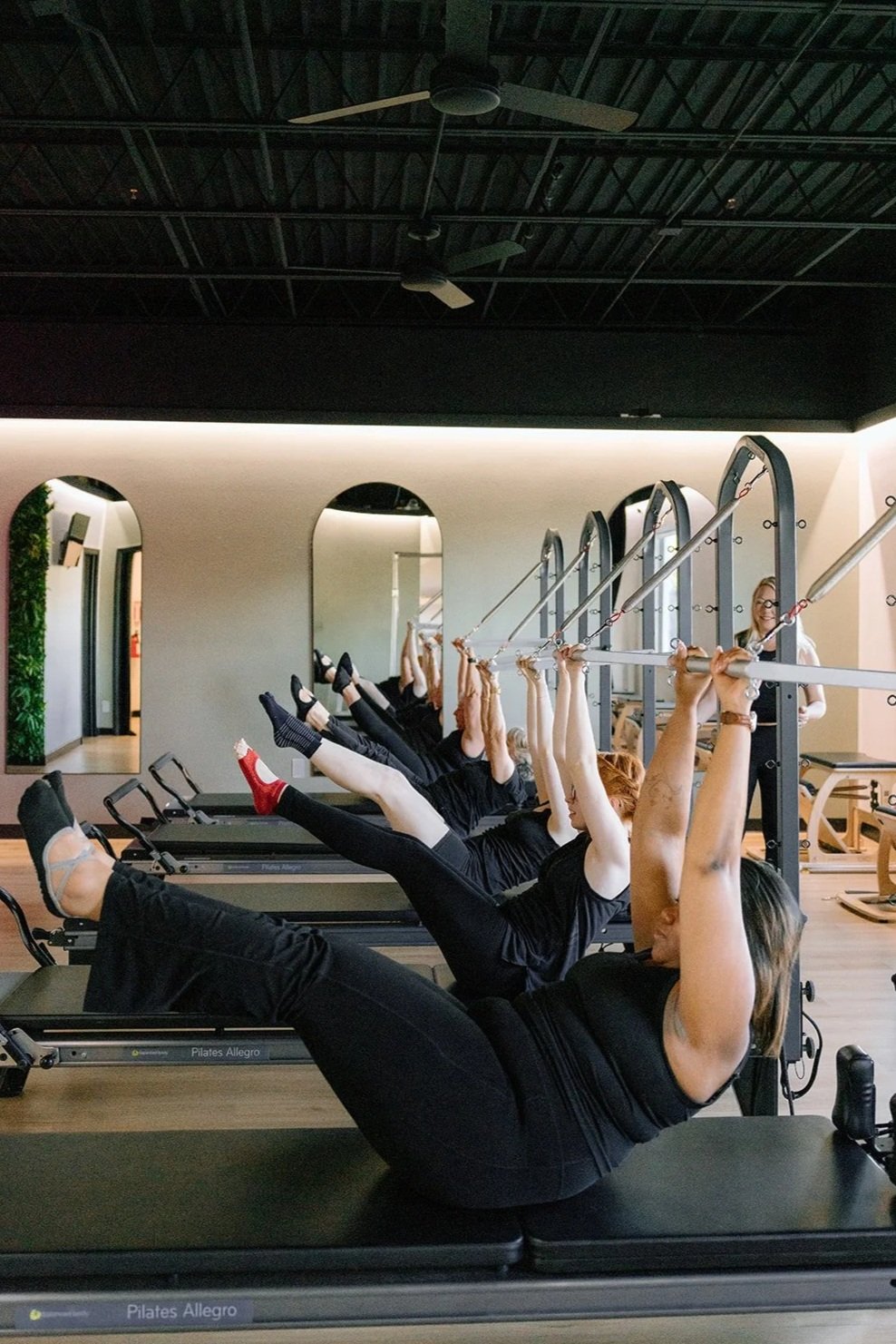 Woman performing Pilates exercise on a reformer chair in a gym.