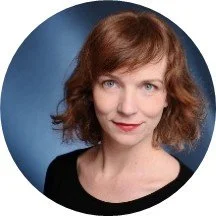 Porträt einer Frau mit braunen lockigen Haaren vor einem blauen Hintergrund.
