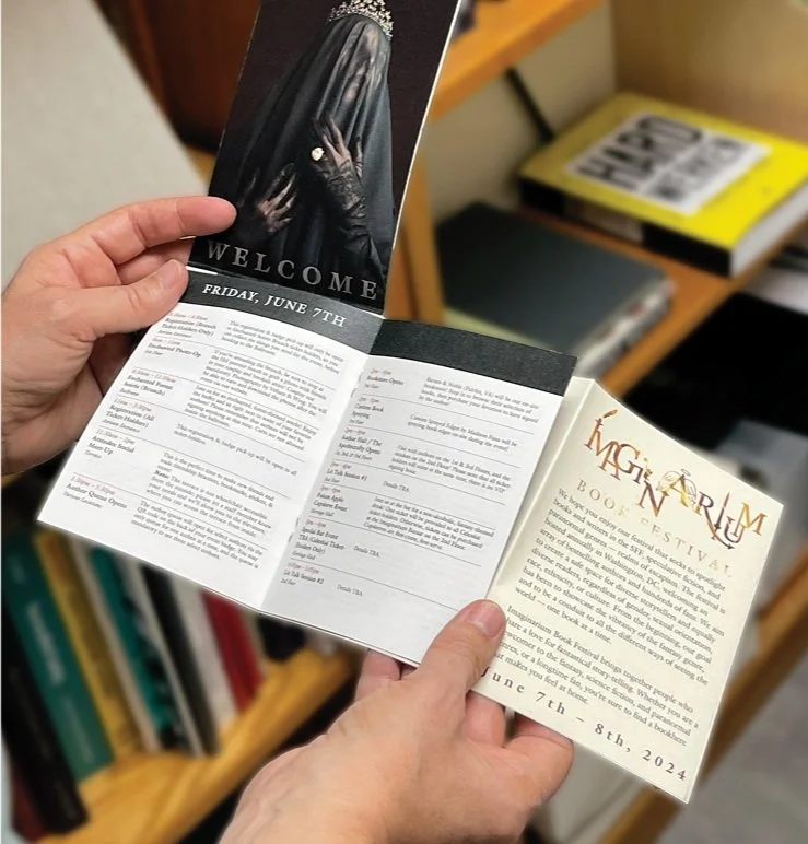 A person holding a program or brochure for a book festival, with various pages visible, including a welcome message and event details, on a bookshelf background.