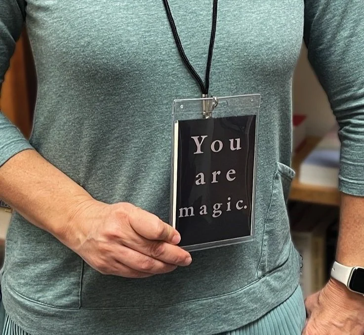 Person wearing a gray hoodie with a motivational badge that reads 'You are magic' hanging around their neck.