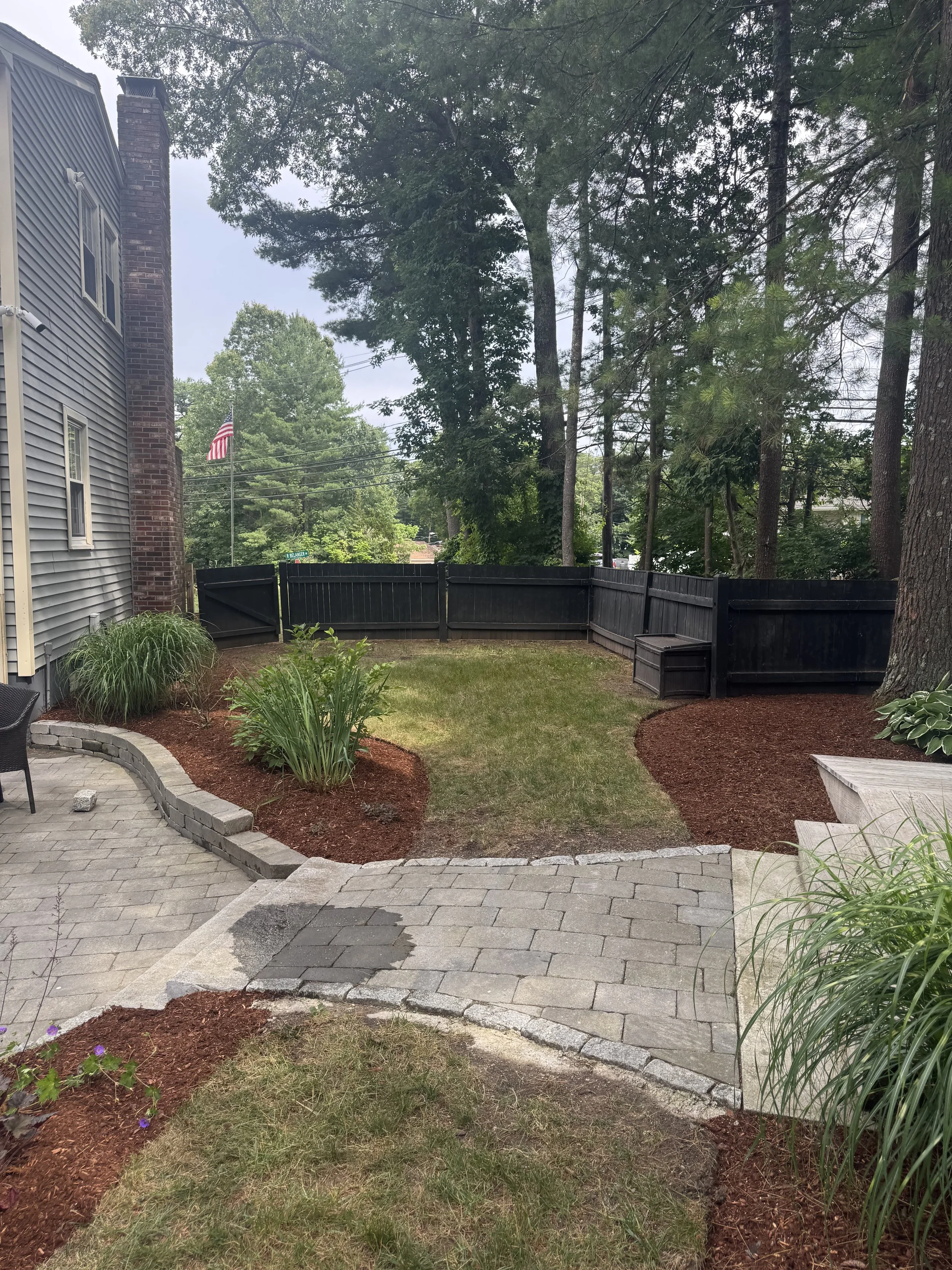 White vinyl fence with lattice top surrounding a grassy yard, bordered by white gravel; trees and houses in the background.