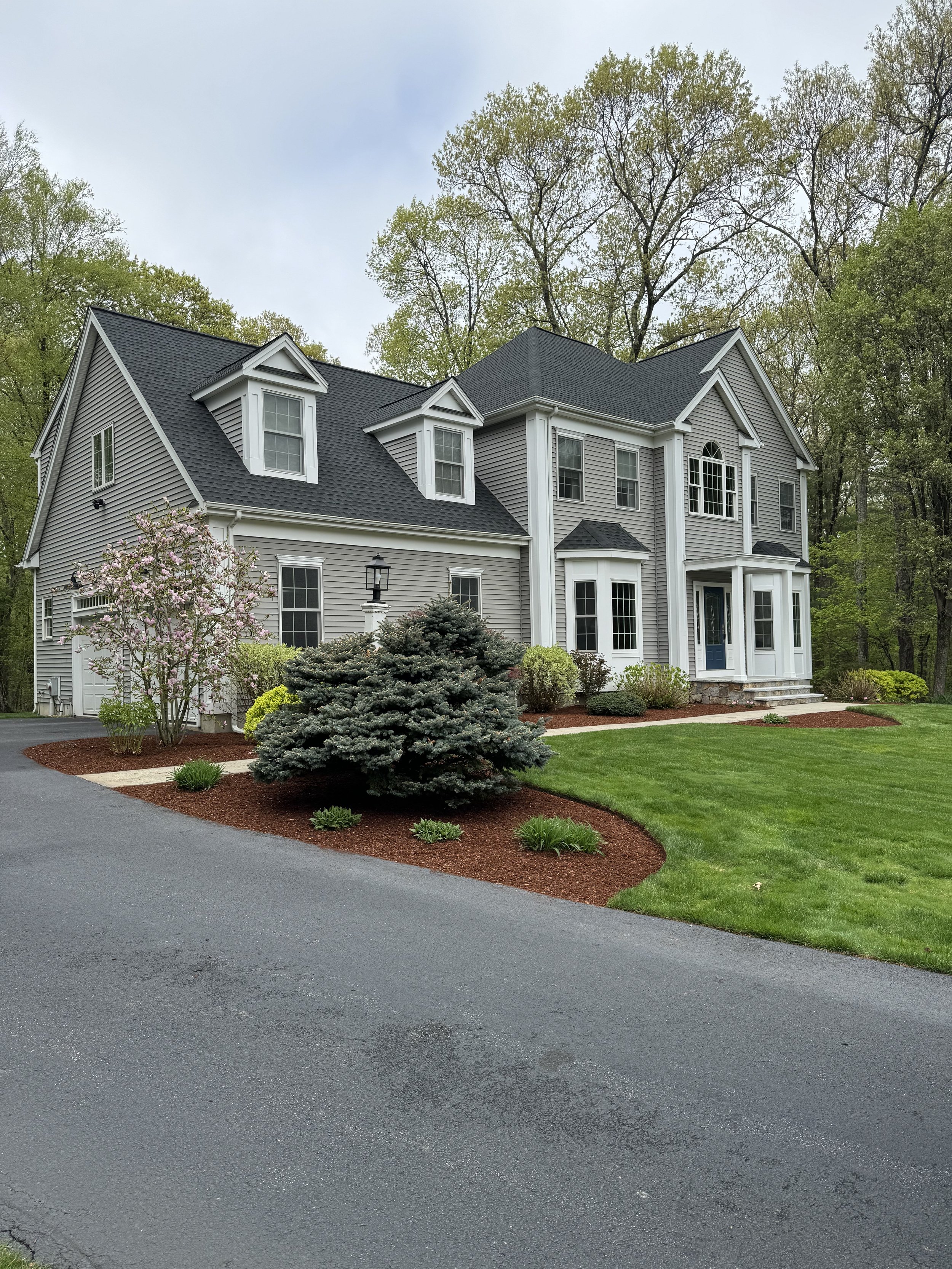 Backyard garden with freshly tilled soil, plants, and a propane tank against a blue siding house.