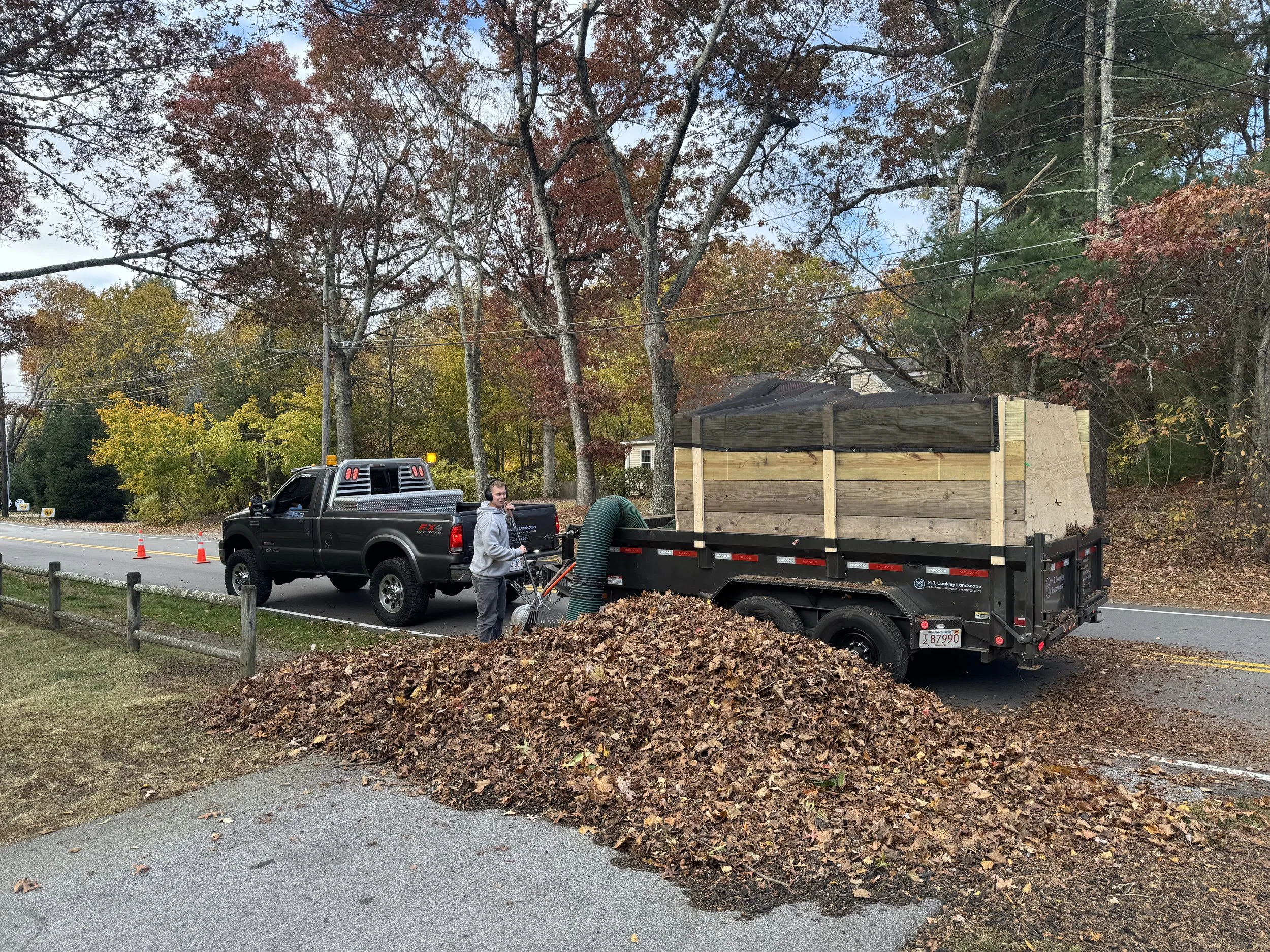 White lattice fence bordering a green lawn with scattered leaves, adjacent to a gravel path, surrounded by trees.