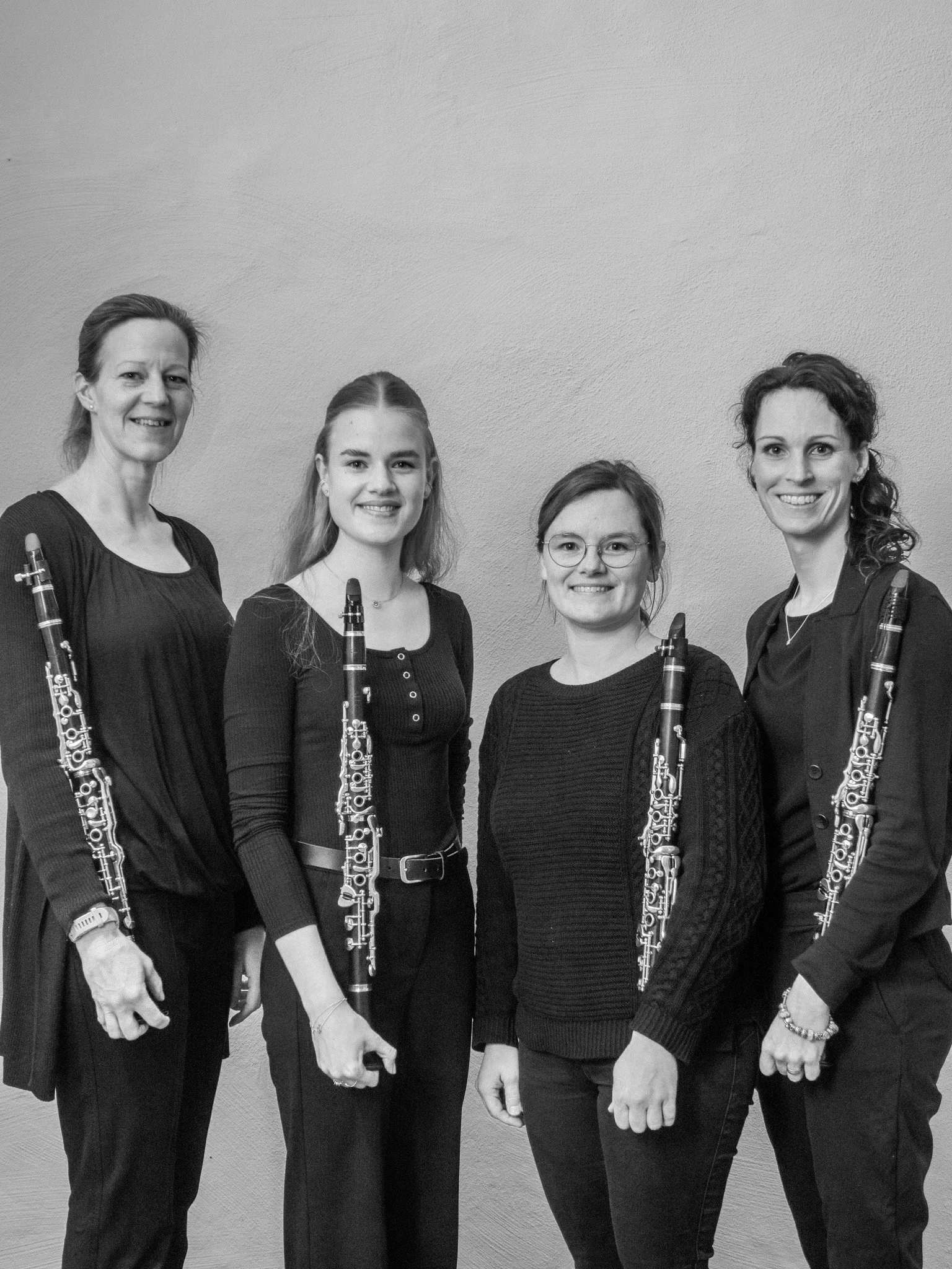Vier Frauen, die Blasinstrumente halten, stehen vor einem neutralen Hintergrund und lächeln in die Kamera. Zwei der Frauen halten Klarinetten.