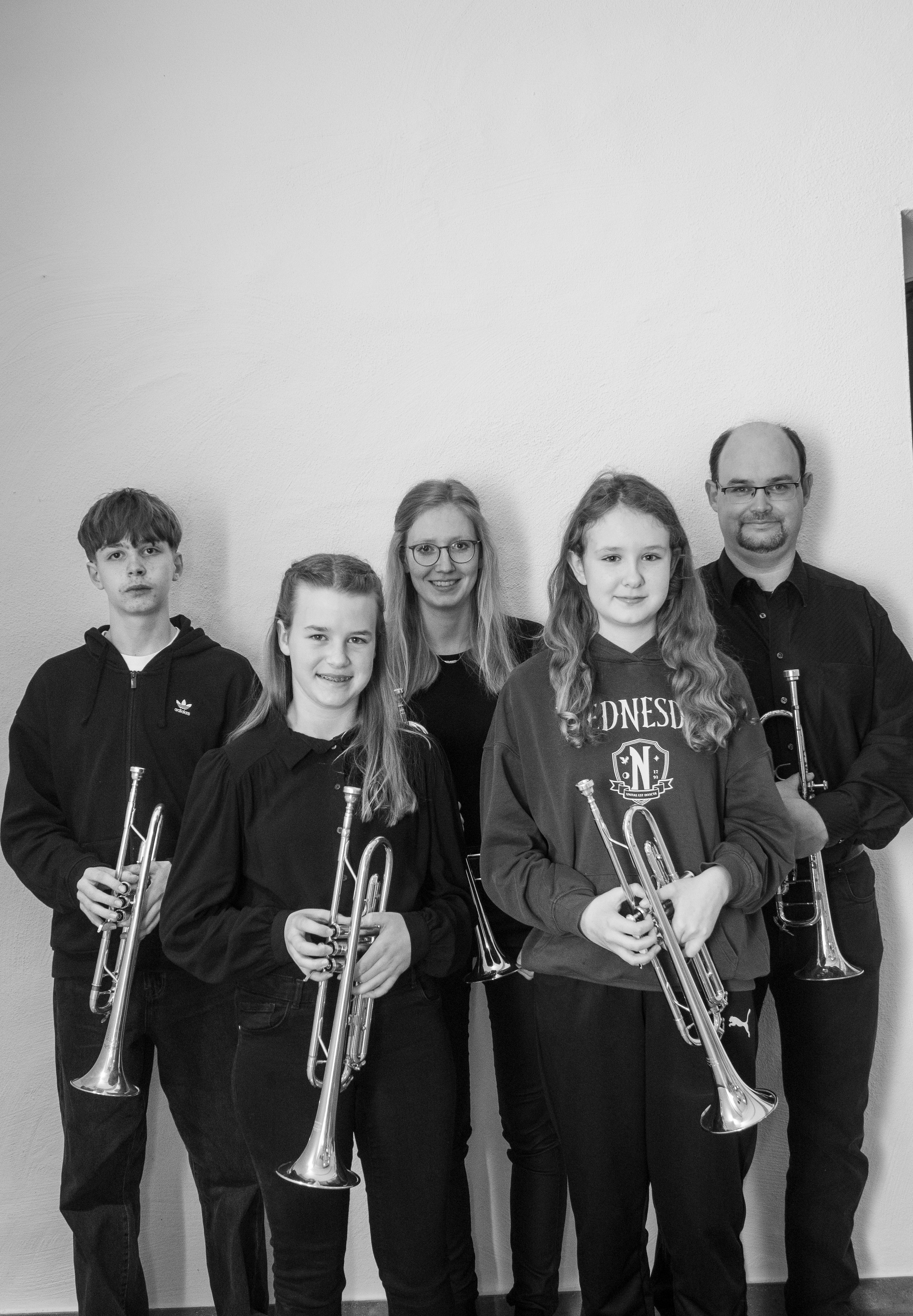 Fünf Personen, die Trompeten halten, stehen vor einer weißen Wand. Alle tragen legere Kleidung und blicken in die Kamera. Es handelt sich um ein Schwarz-Weiß-Foto.