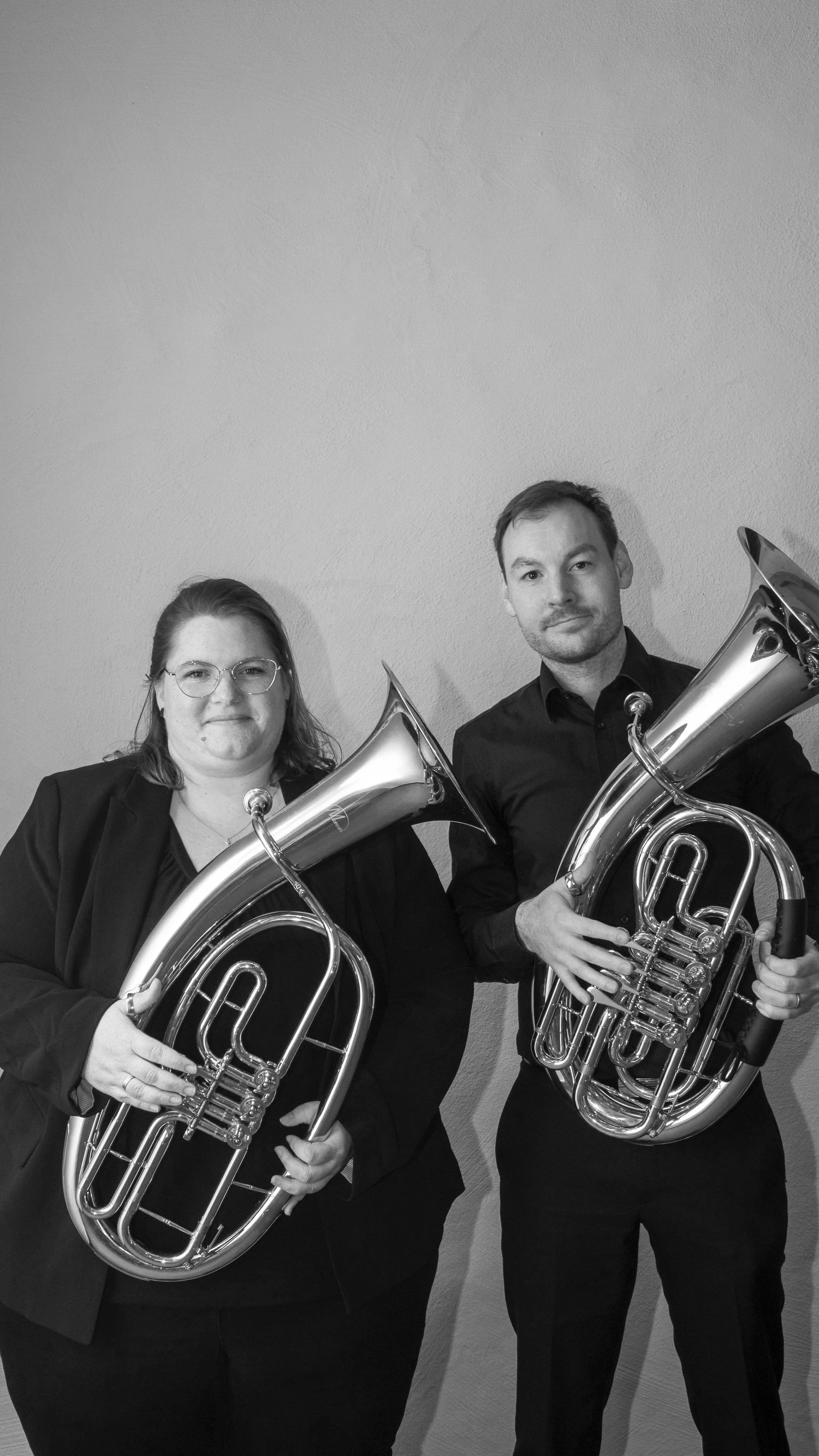 Zwei Personen, die Blechblasinstrumente (Euphonien) halten, vor einem neutralen Hintergrund.