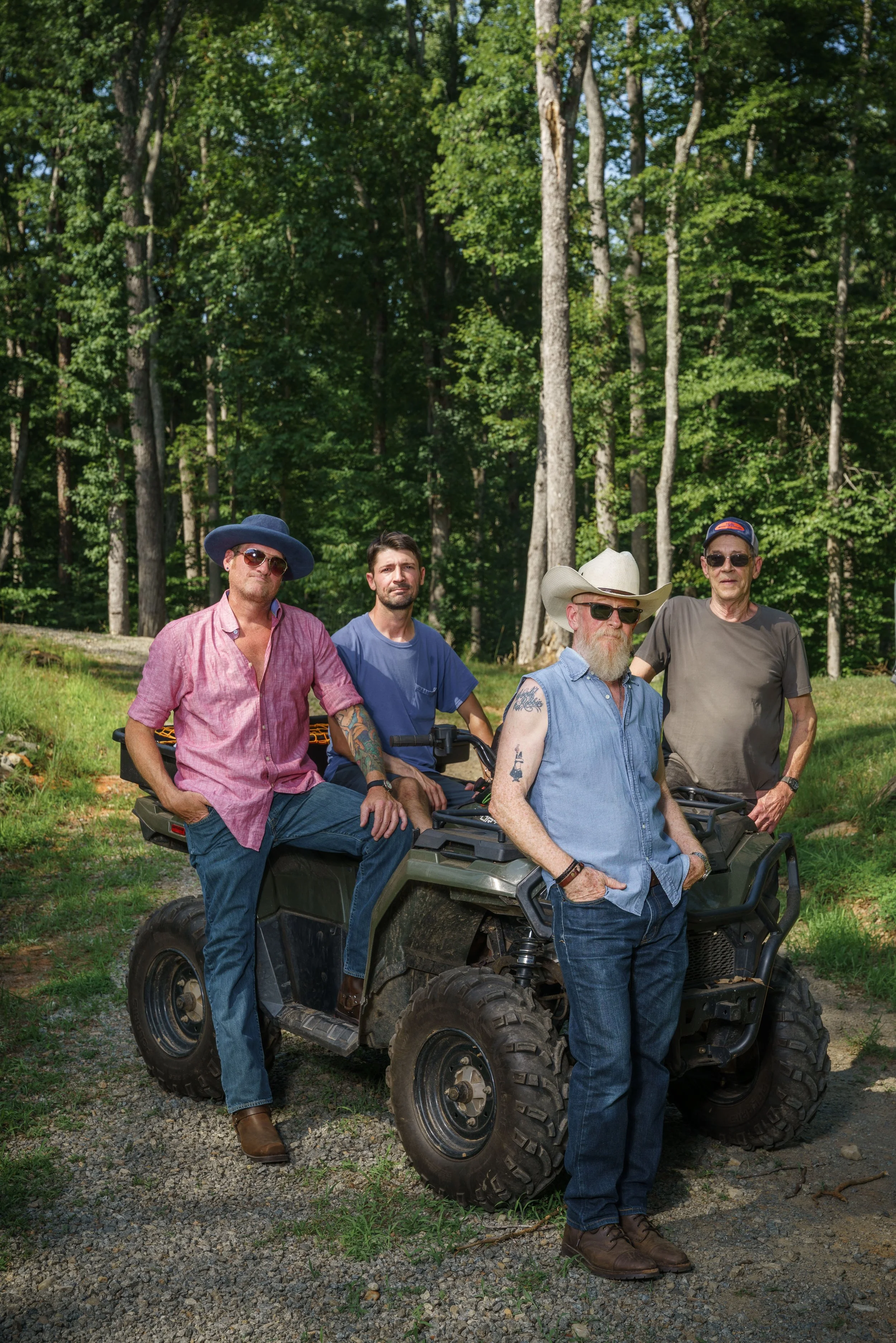 The 10-4 Good Buddies at Buck Naked Hunt Camp beside a four-wheeler vehicle in a wooded area, some wearing sunglasses and hats, dressed casually.
