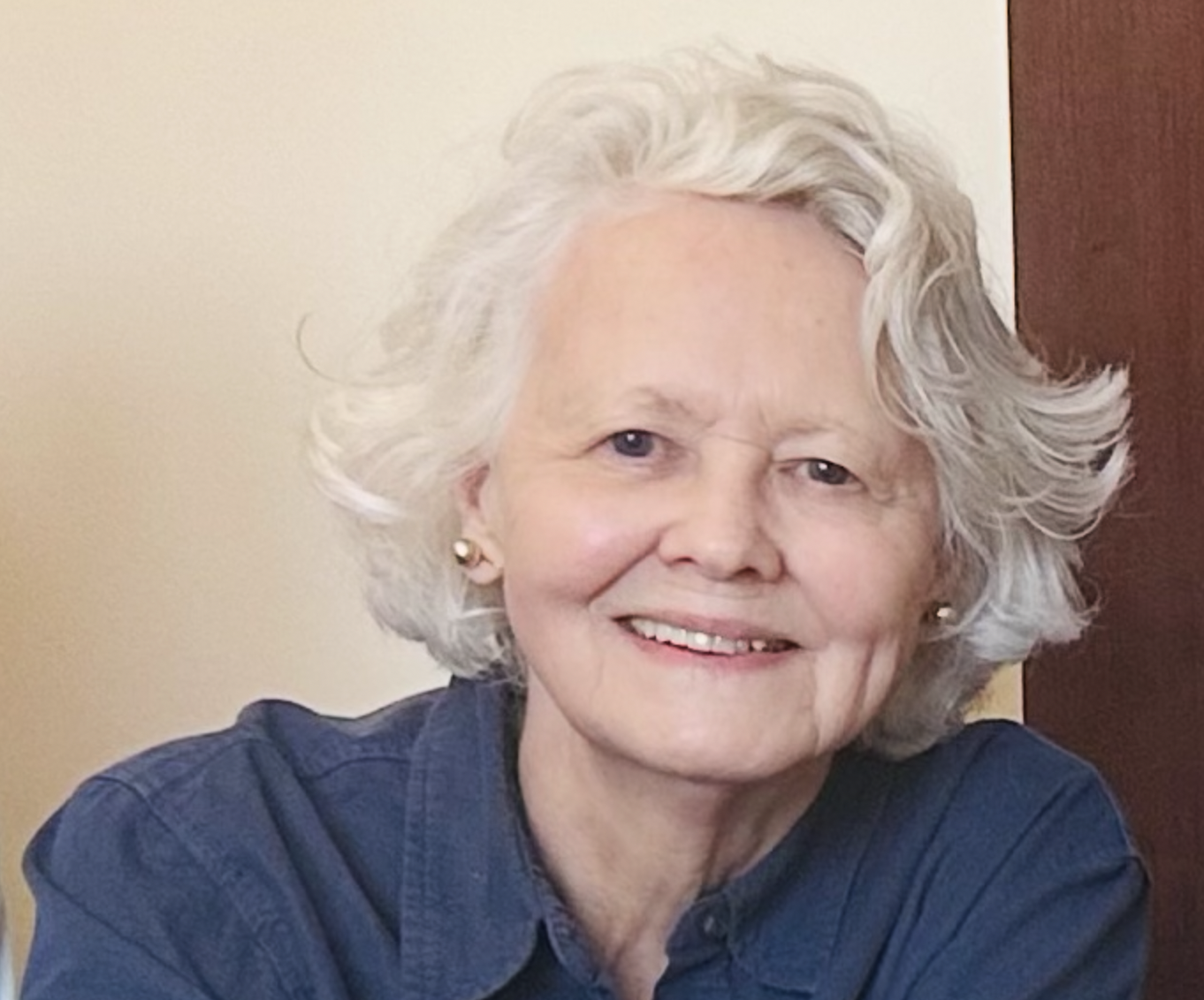 Smiling senior woman with gray hair wearing a dark blue shirt and pearl earrings.