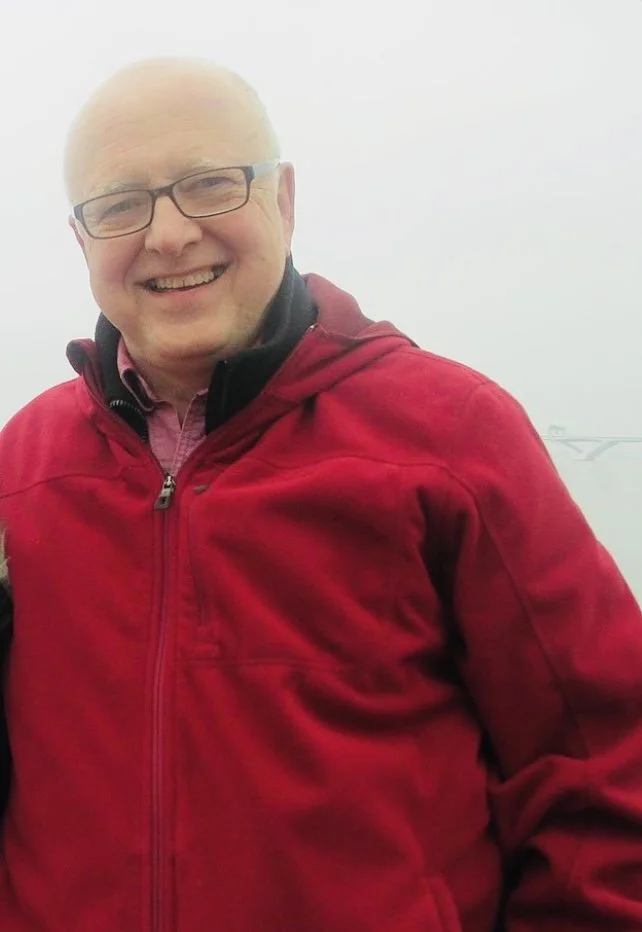 Man wearing glasses and a red jacket, smiling at the camera.