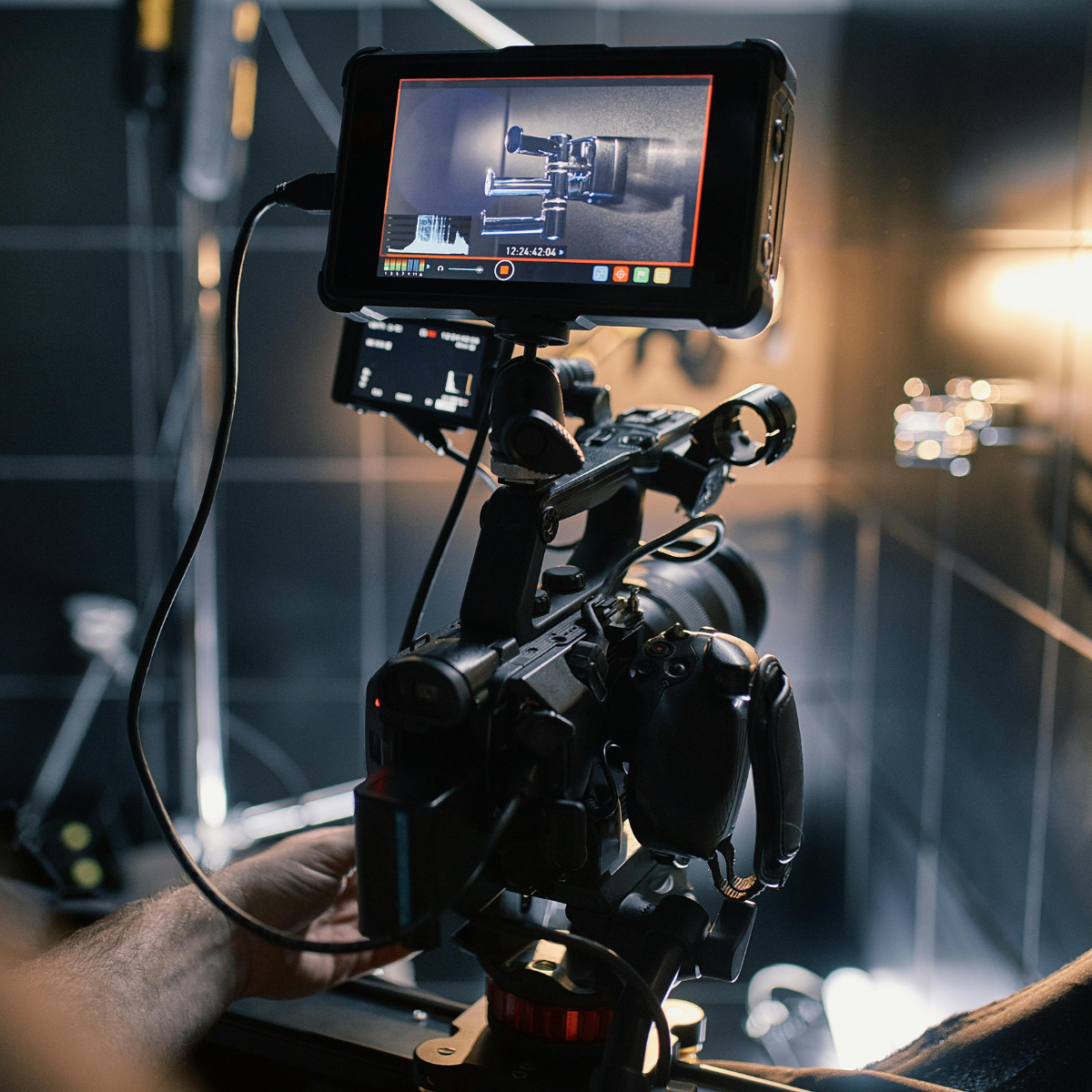 A professional camera setup on a tripod with an external monitor displaying a close-up shot of a metallic object on a dark background.