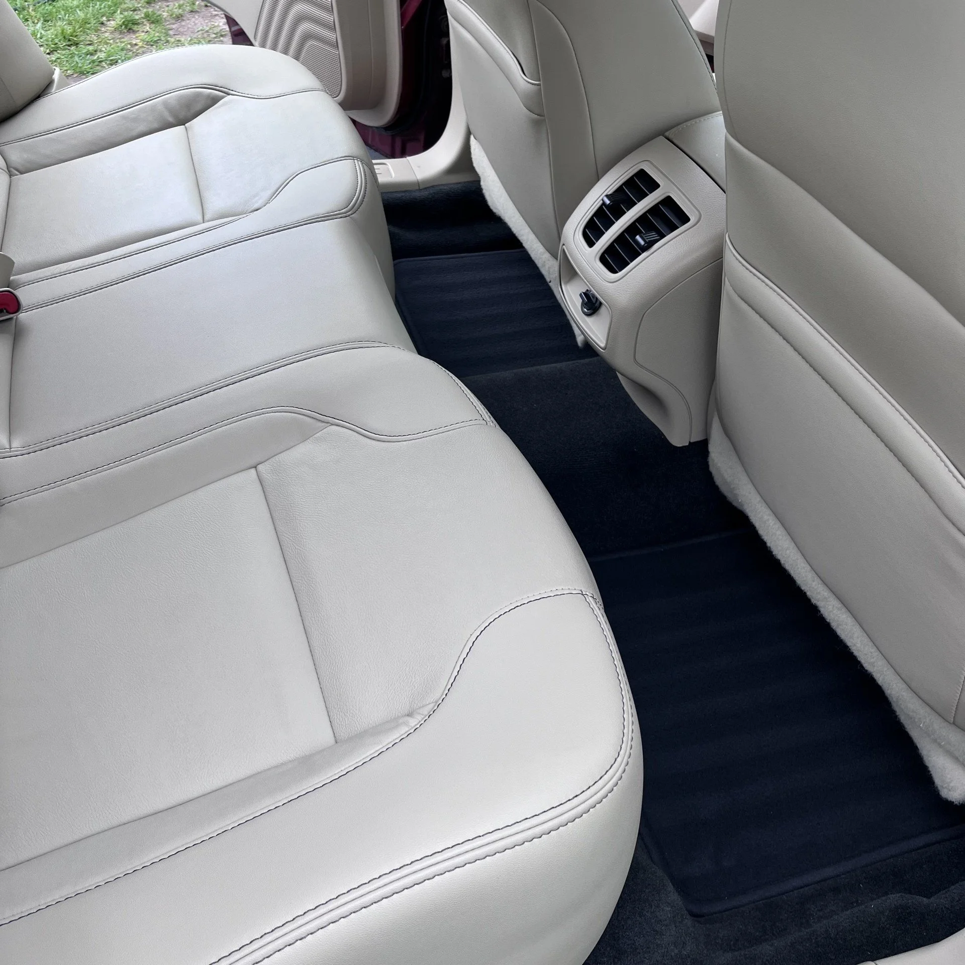 Backseat area of a car with light-colored leather seats, black floor mats, and rear air conditioning vents.