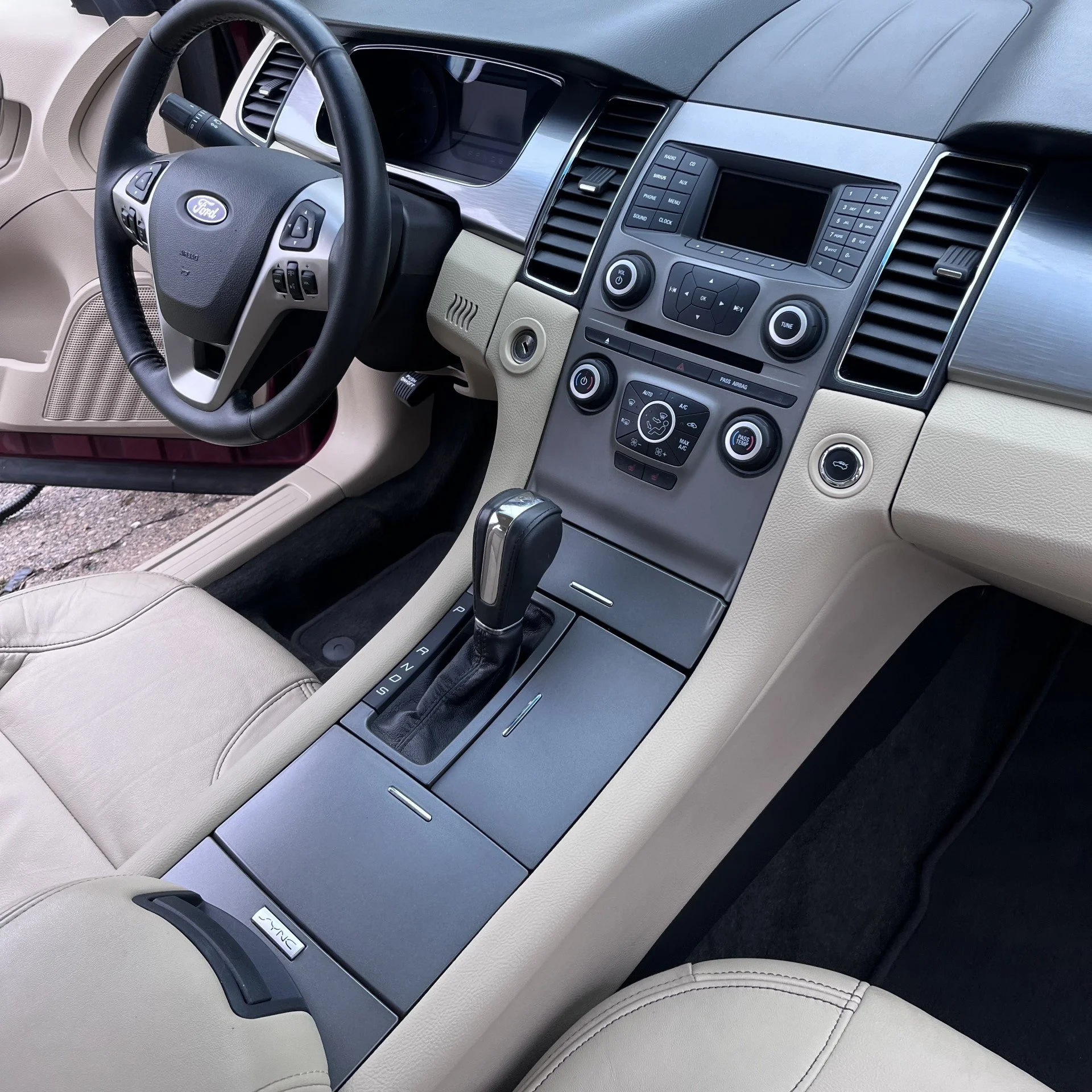 Interior view of a beige Ford vehicle with a gear shifter, control buttons, and a steering wheel.