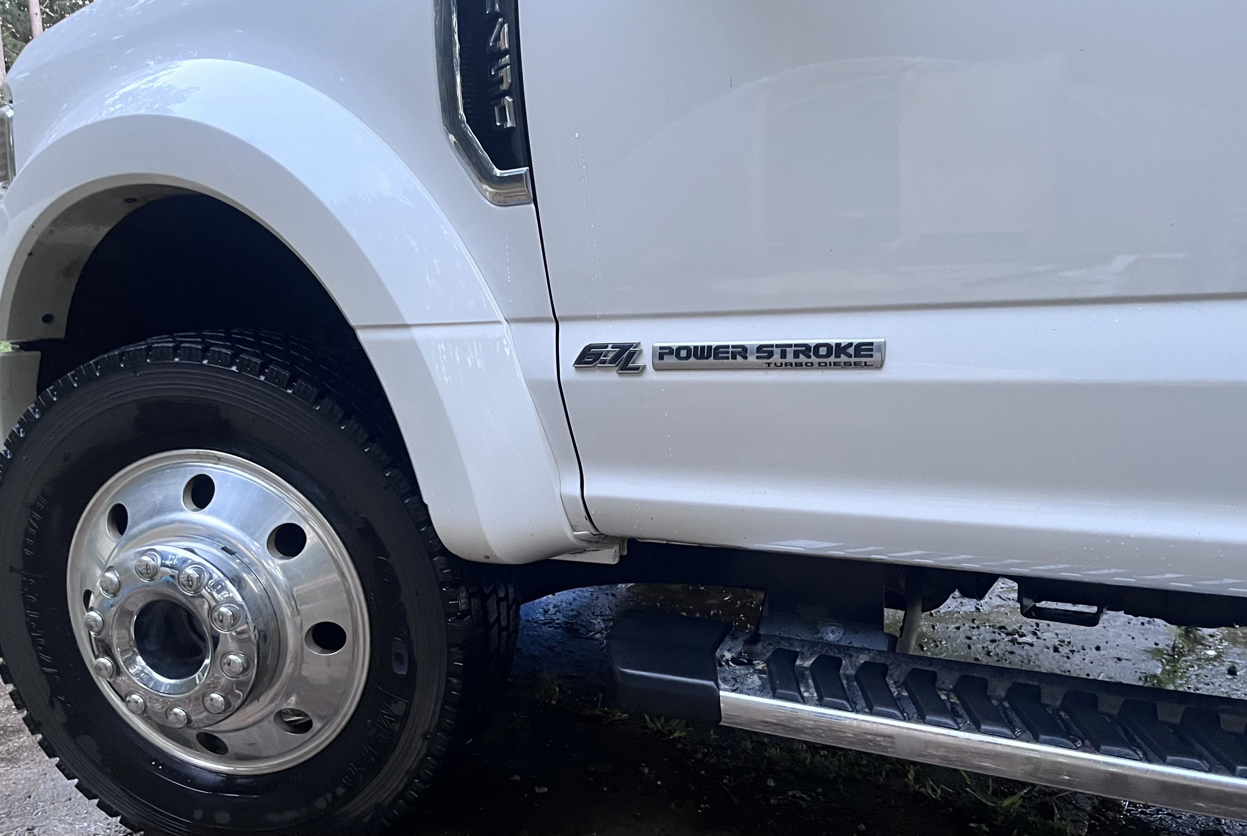 Close-up of a white truck's front wheel and side badge that reads '6.7L Power Stroke Turbo Diesel'.