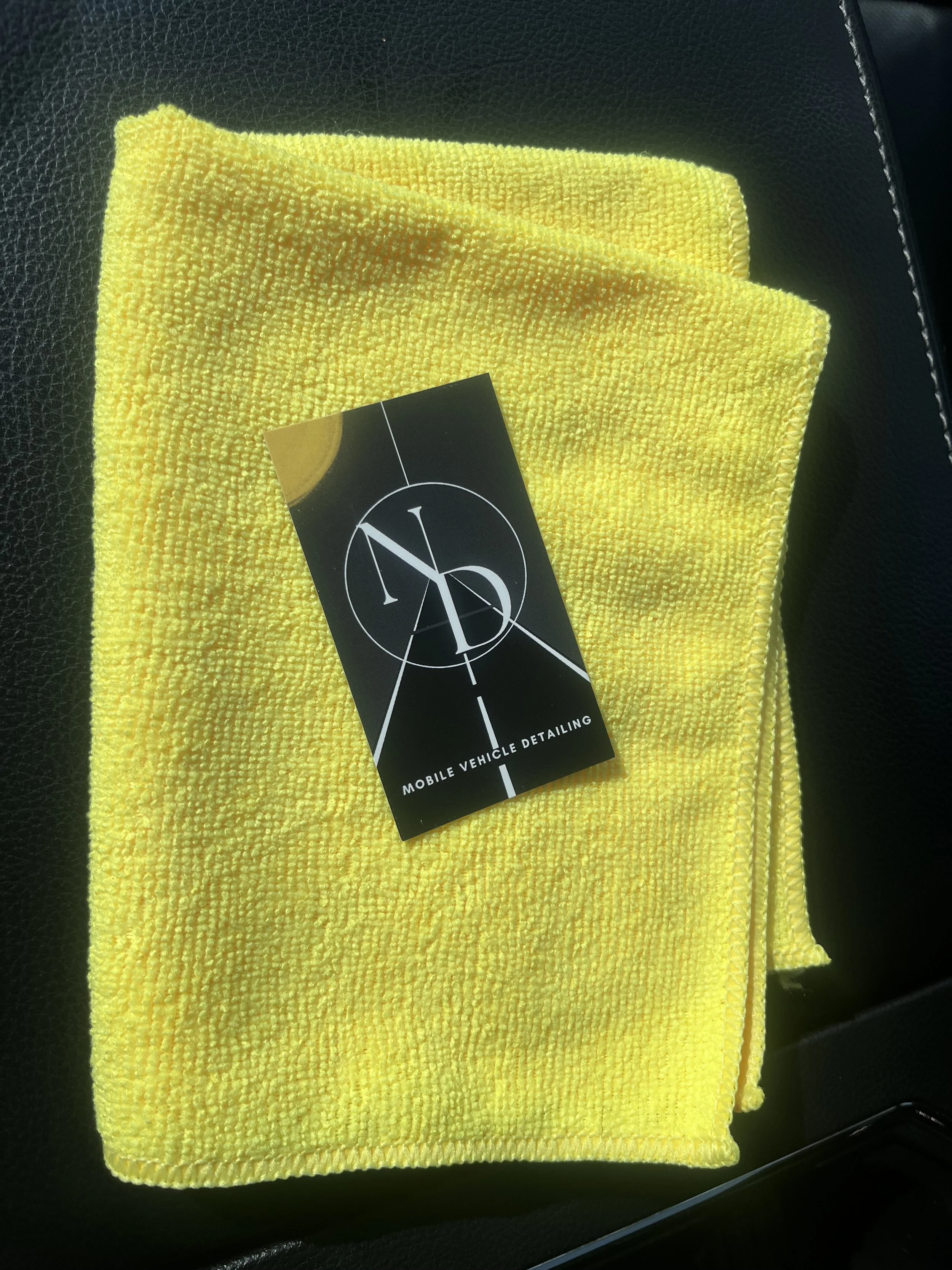 A yellow microfiber cloth with a black business card labeled 'Mobile Vehicle Detailing' resting on top of it.