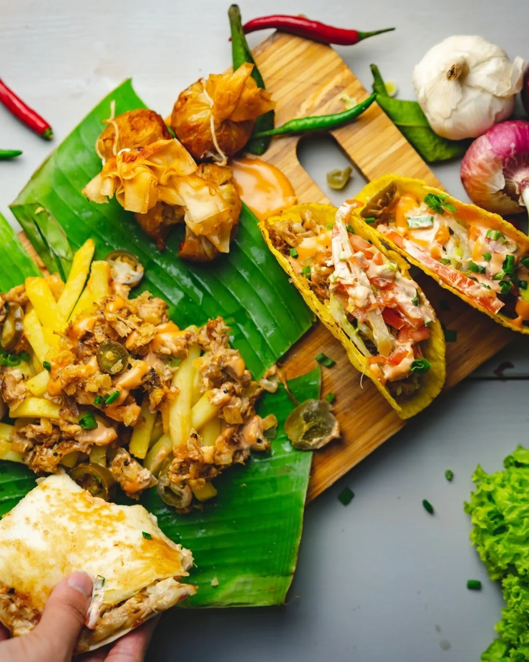 A hand pouring champagne into a glass amidst many empty champagne glasses on a wooden table.