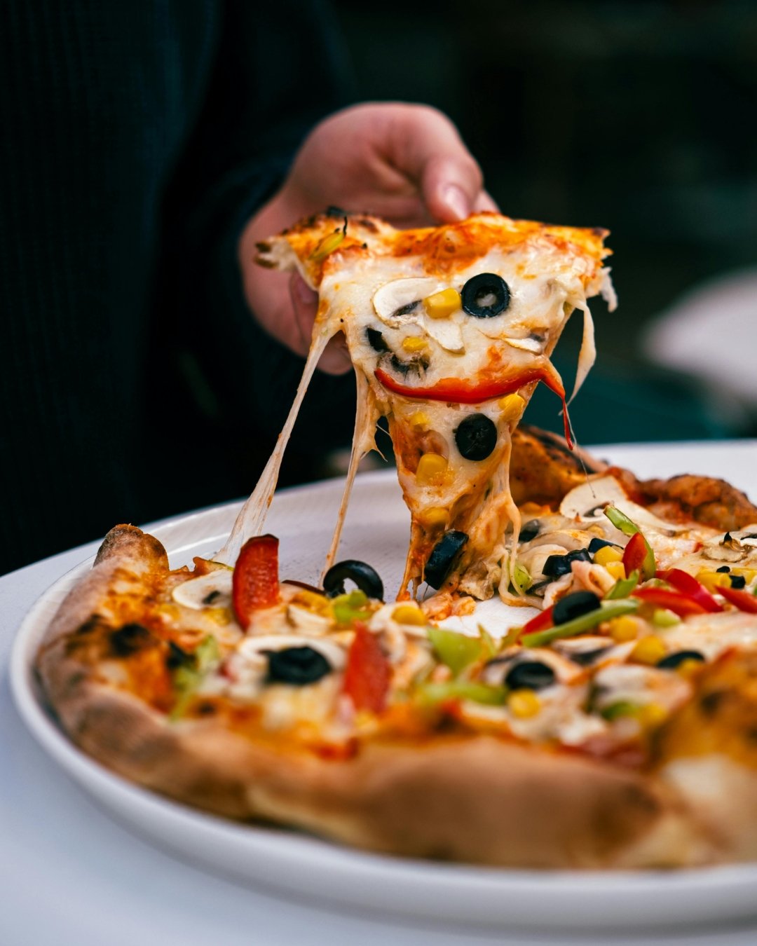 Close-up of two pizzas with melted cheese and toppings. The top pizza has spinach leaves and a white sauce, while the bottom pizza has sausage, potatoes, and cheese.