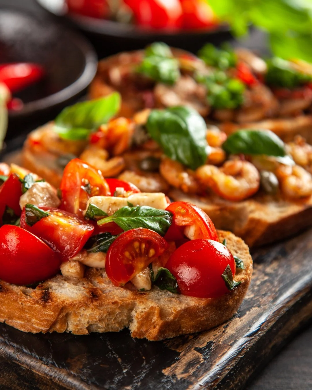 Close-up of toasted bread slices topped with creamy chicken salad, garnished with onion rings and fresh herbs, on a wooden platter.