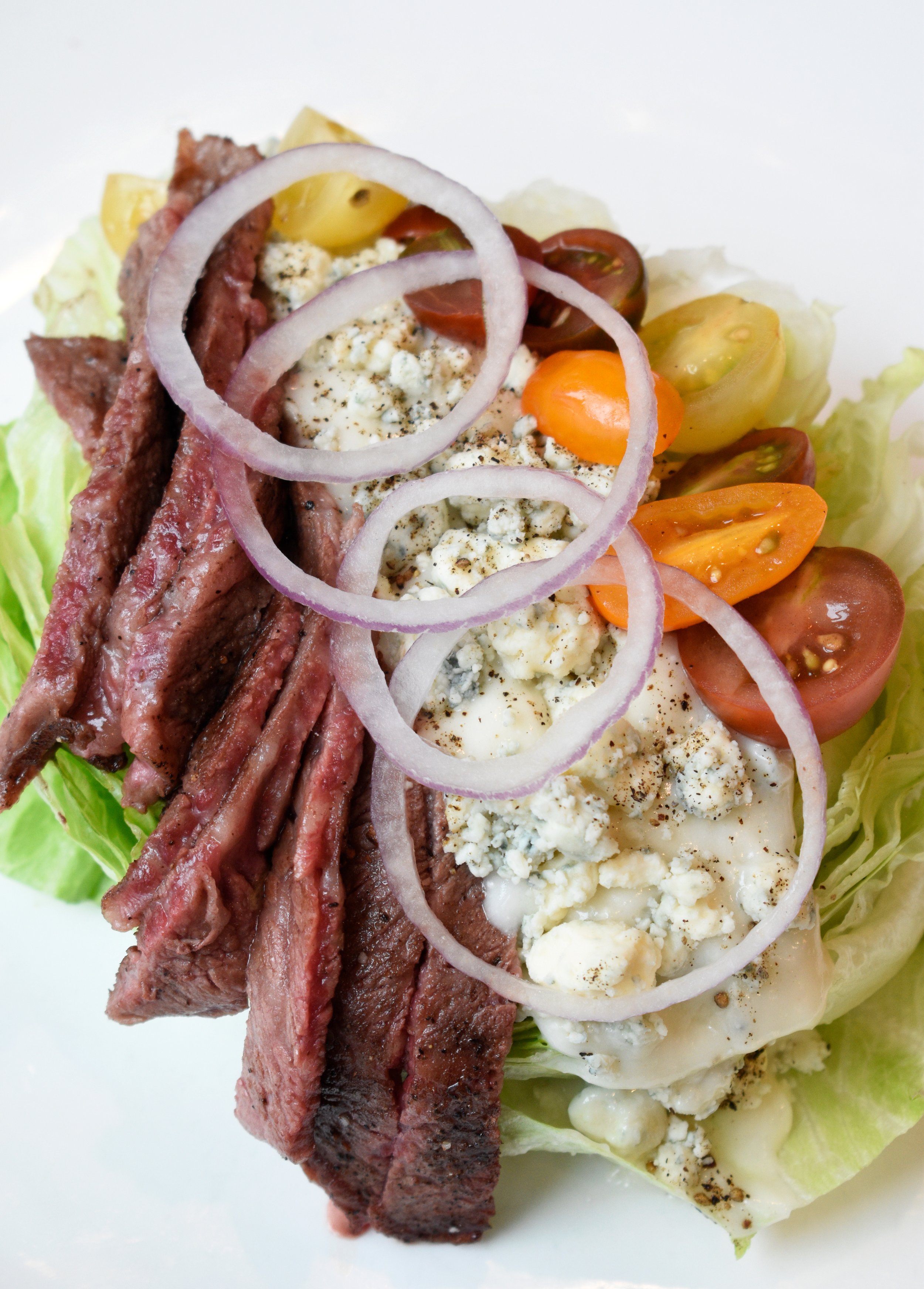 Salad with sliced steak, cherry tomatoes, blue cheese crumbles, sliced red onions, lettuce, and a creamy dressing