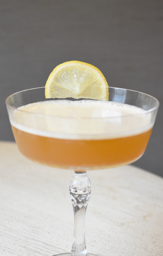 Cocktail in a stemmed glass with a lemon wedge garnish.