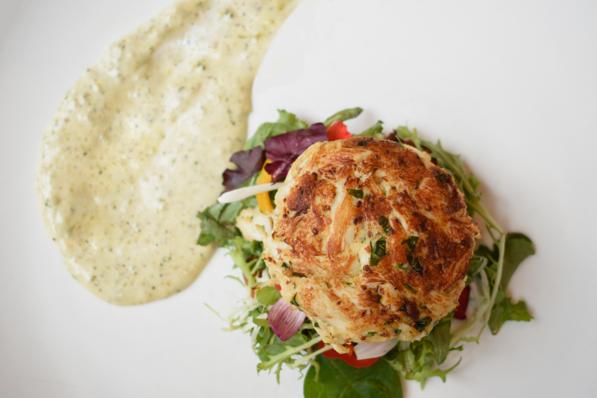Baked crab cake on mixed greens salad with house-made dressing on white plate