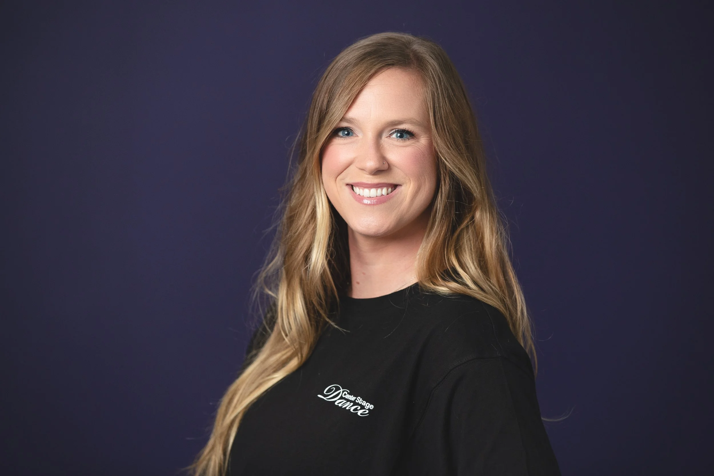 A photo of Abby Ellis smiling at the camera in front of a purple backdrop.