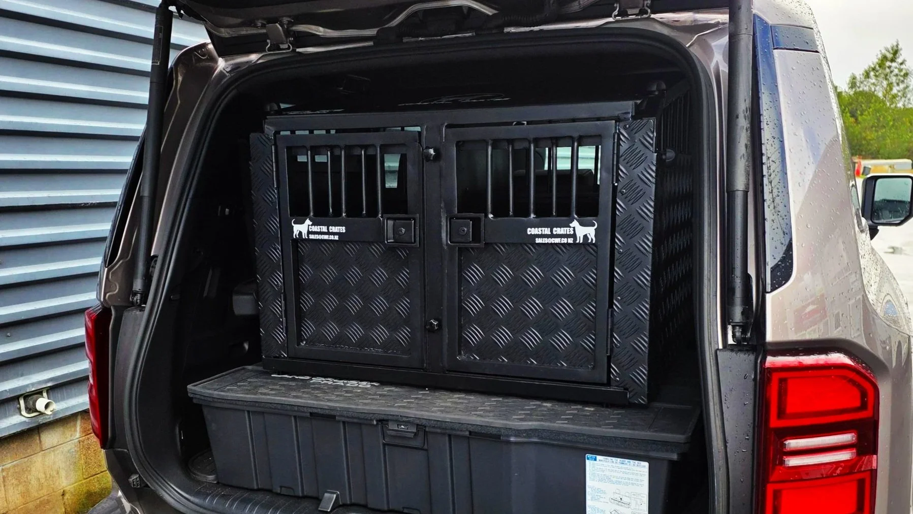 The back of a black SUV with its trunk open, showing a black pet crate with metal bars inside.