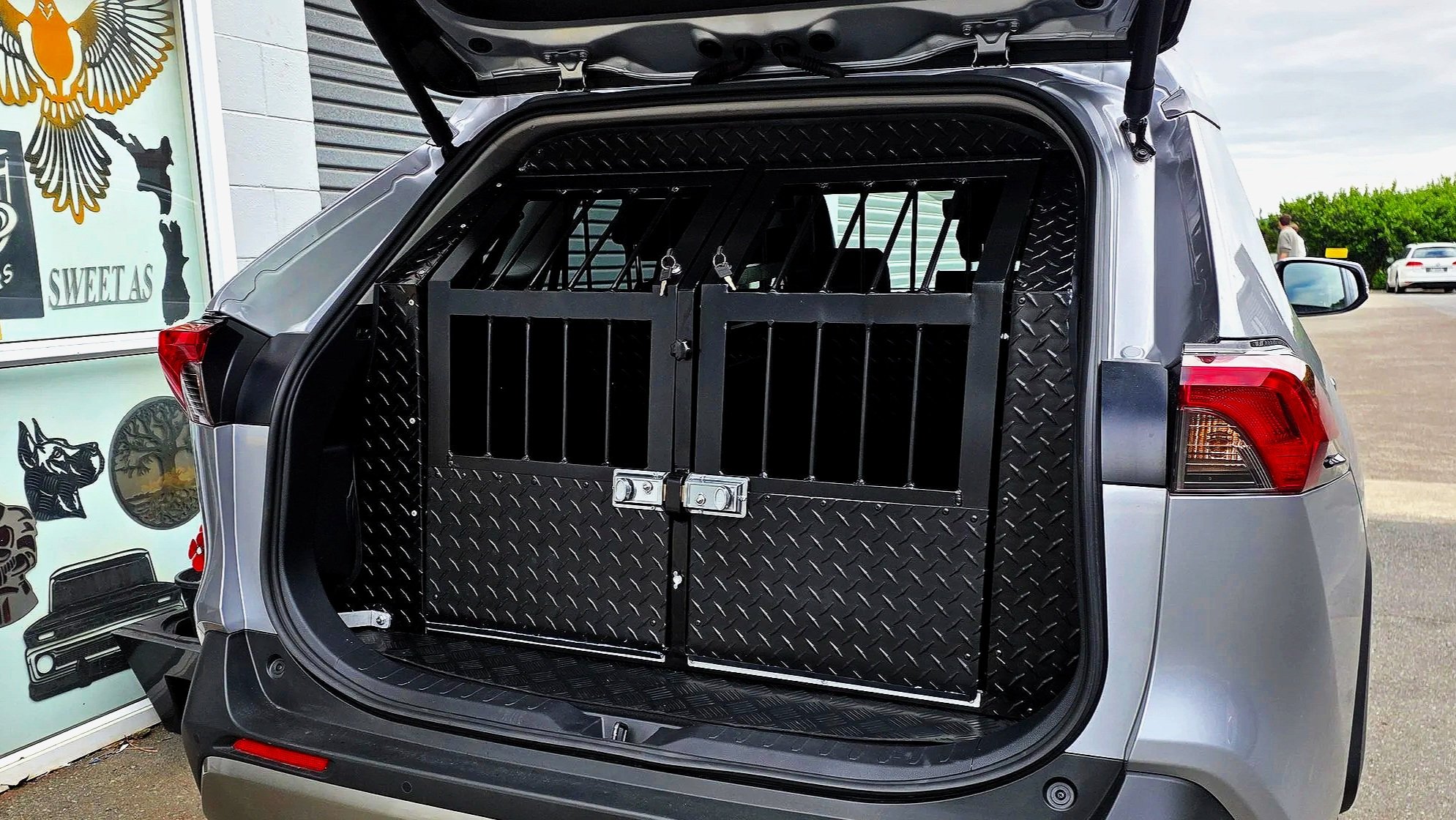 The back of a silver vehicle with the hatch open, revealing a black metal dog crate inside.