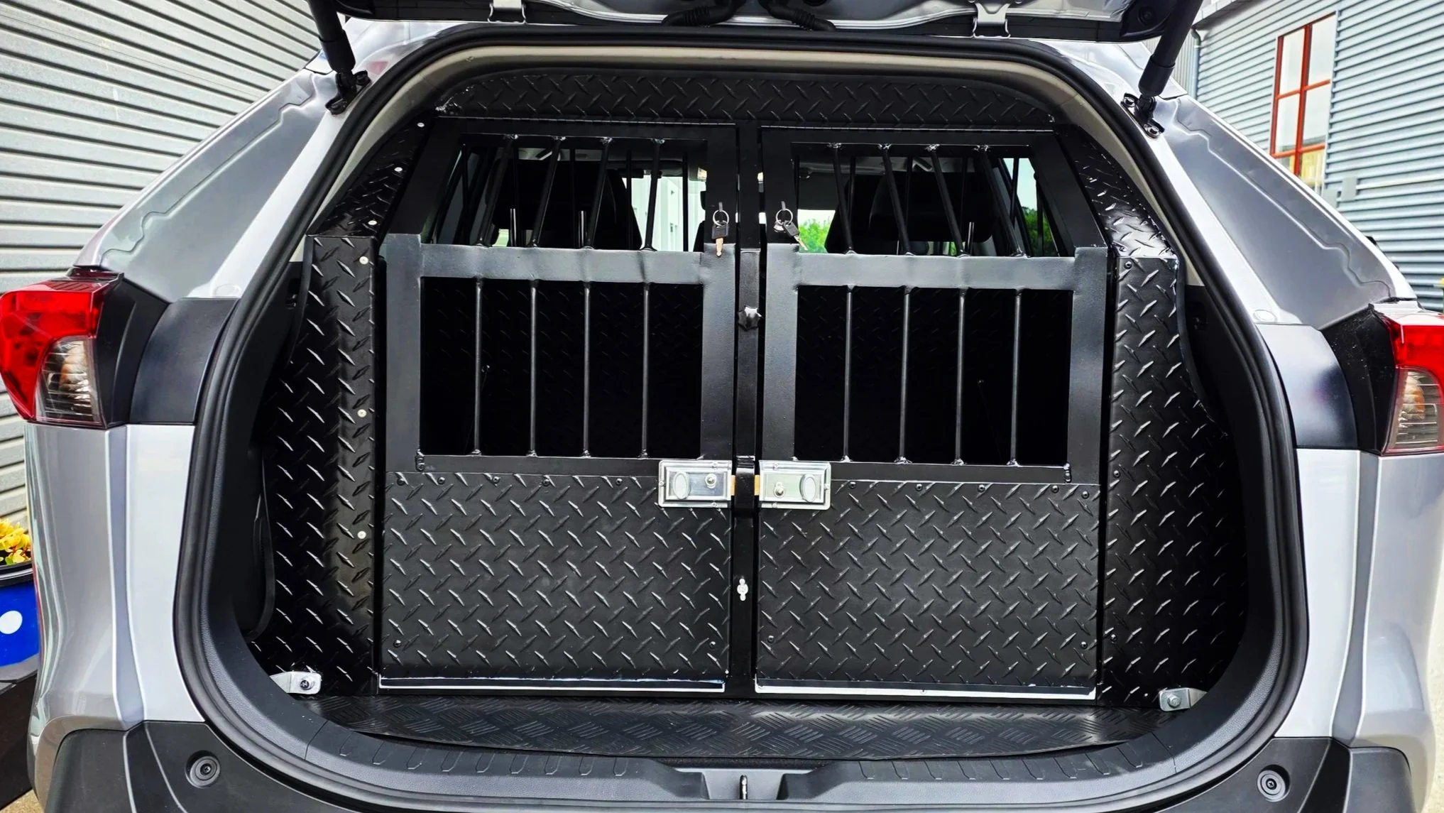 The open rear of a silver police SUV shows a black partition with vertical bars, and double doors with two locks.