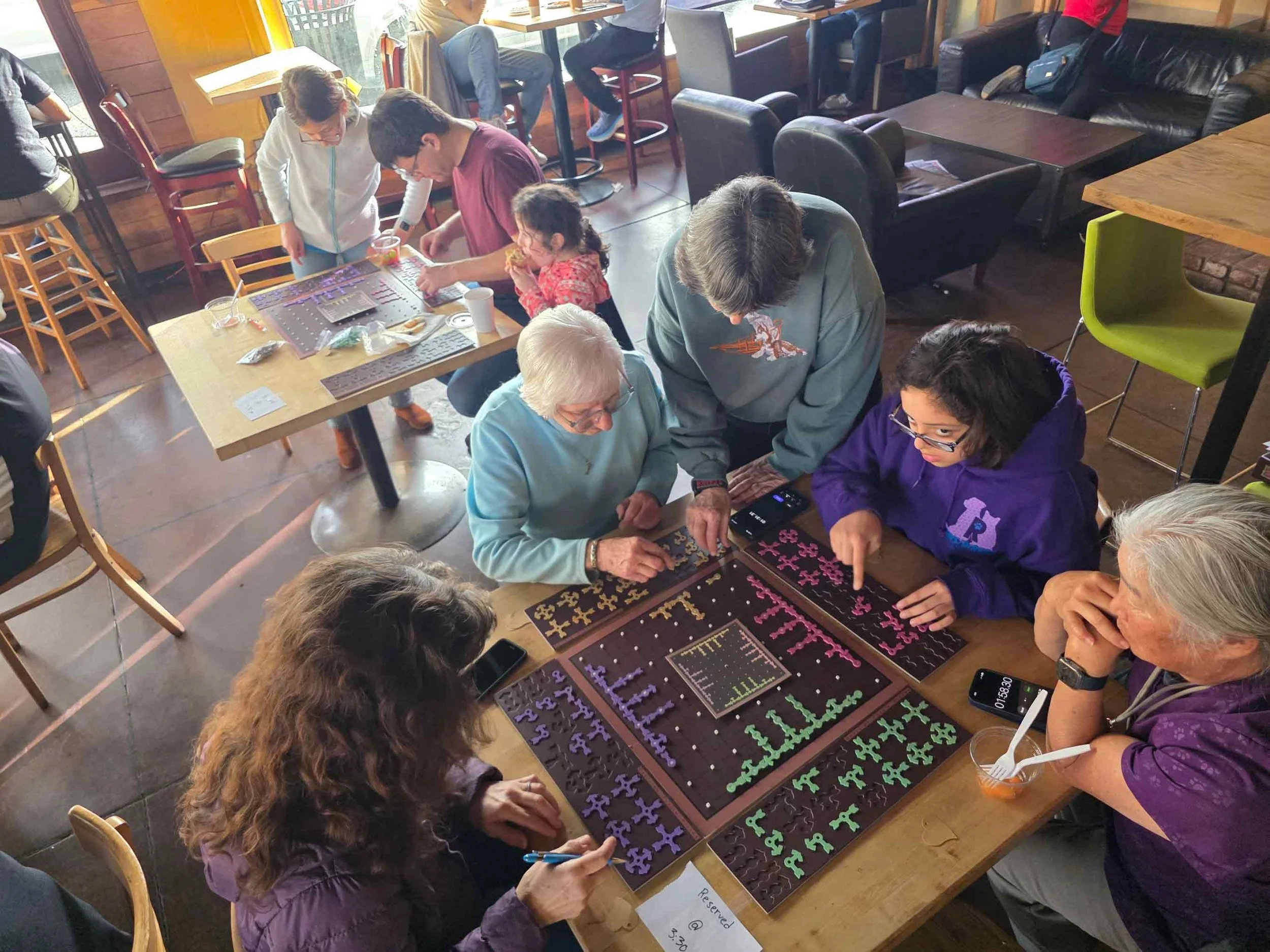 A group of people playing a board game called Geozzle with colored puzzle pieces on a table inside a restaurant or cafe.