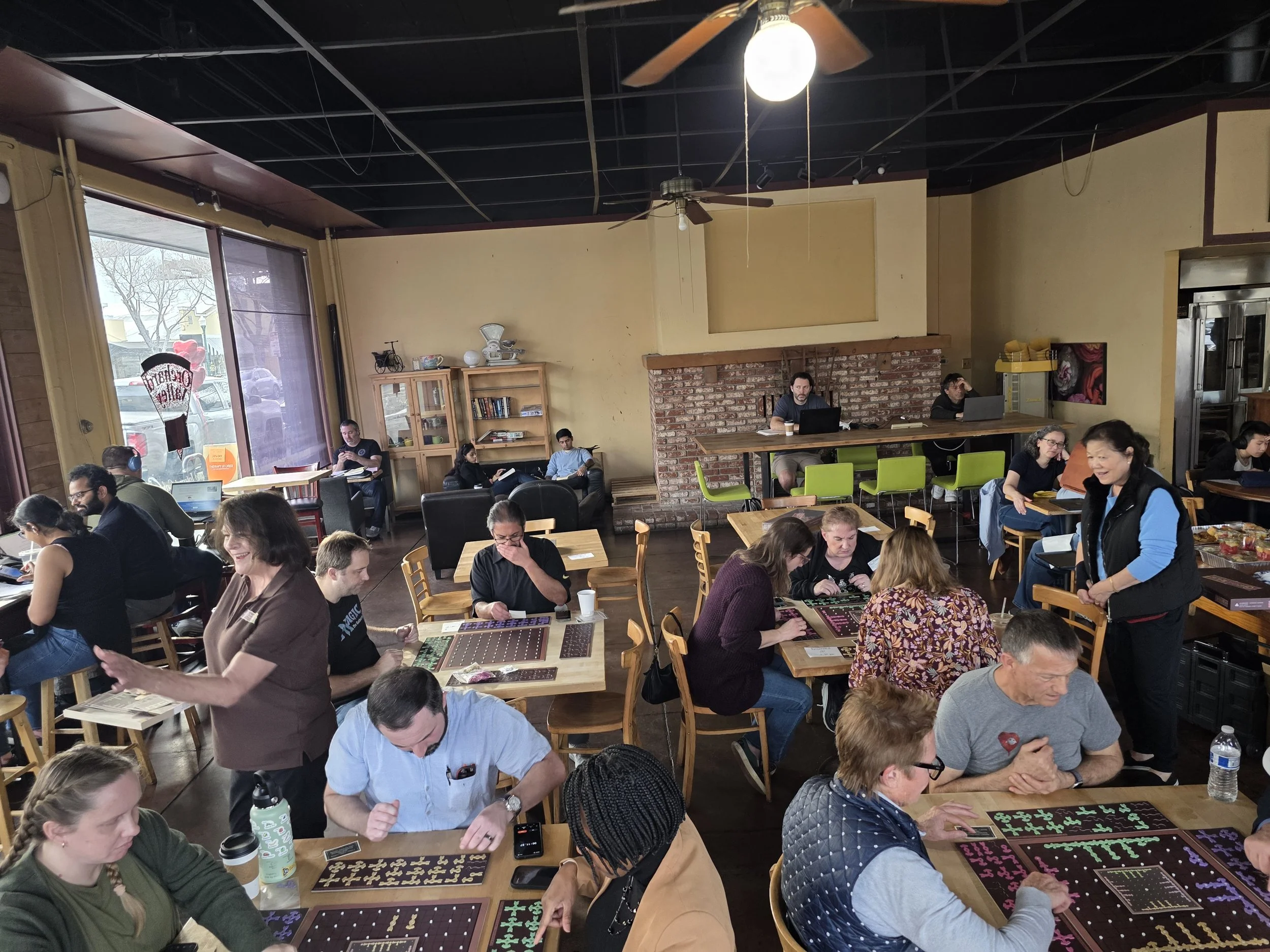People playing Geozzle board game at tables in a coffee shop or casual venue.