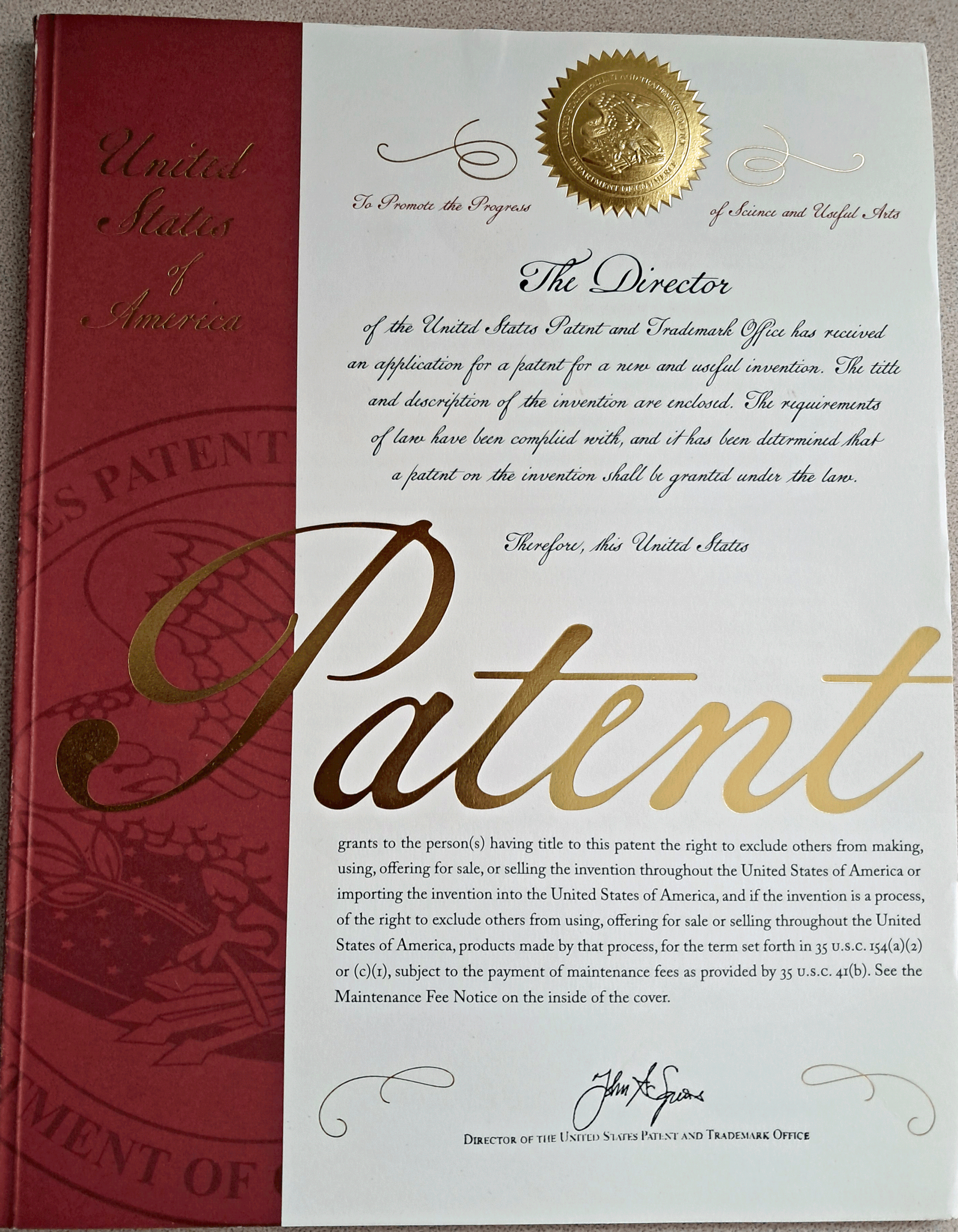 Close-up of a United States patent document with a red and gold cover, a gold embossed seal, and handwritten signatures.