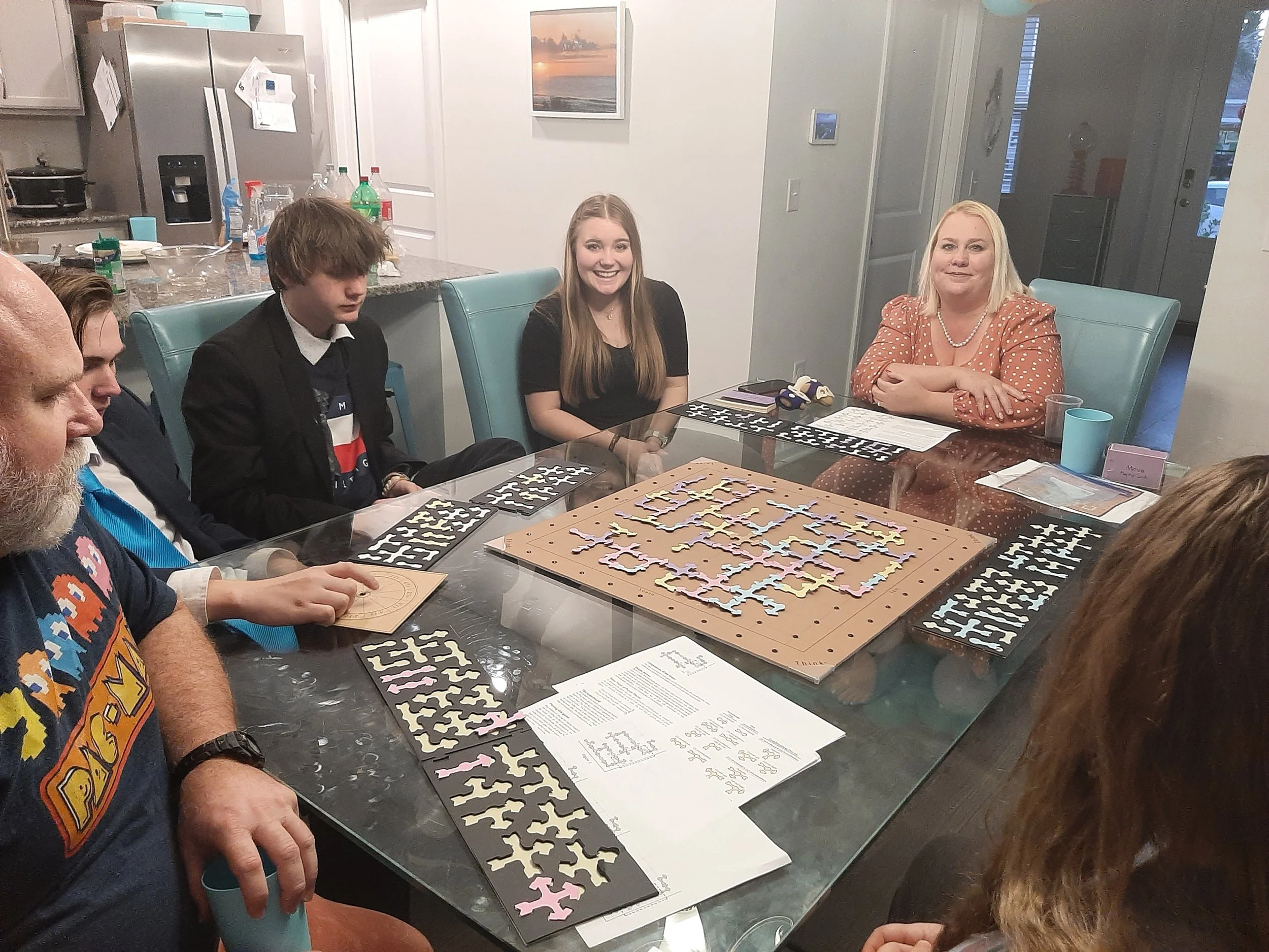 People sitting around a dining table playing a puzzle game with puzzle pieces and pattern sheets in front of them.