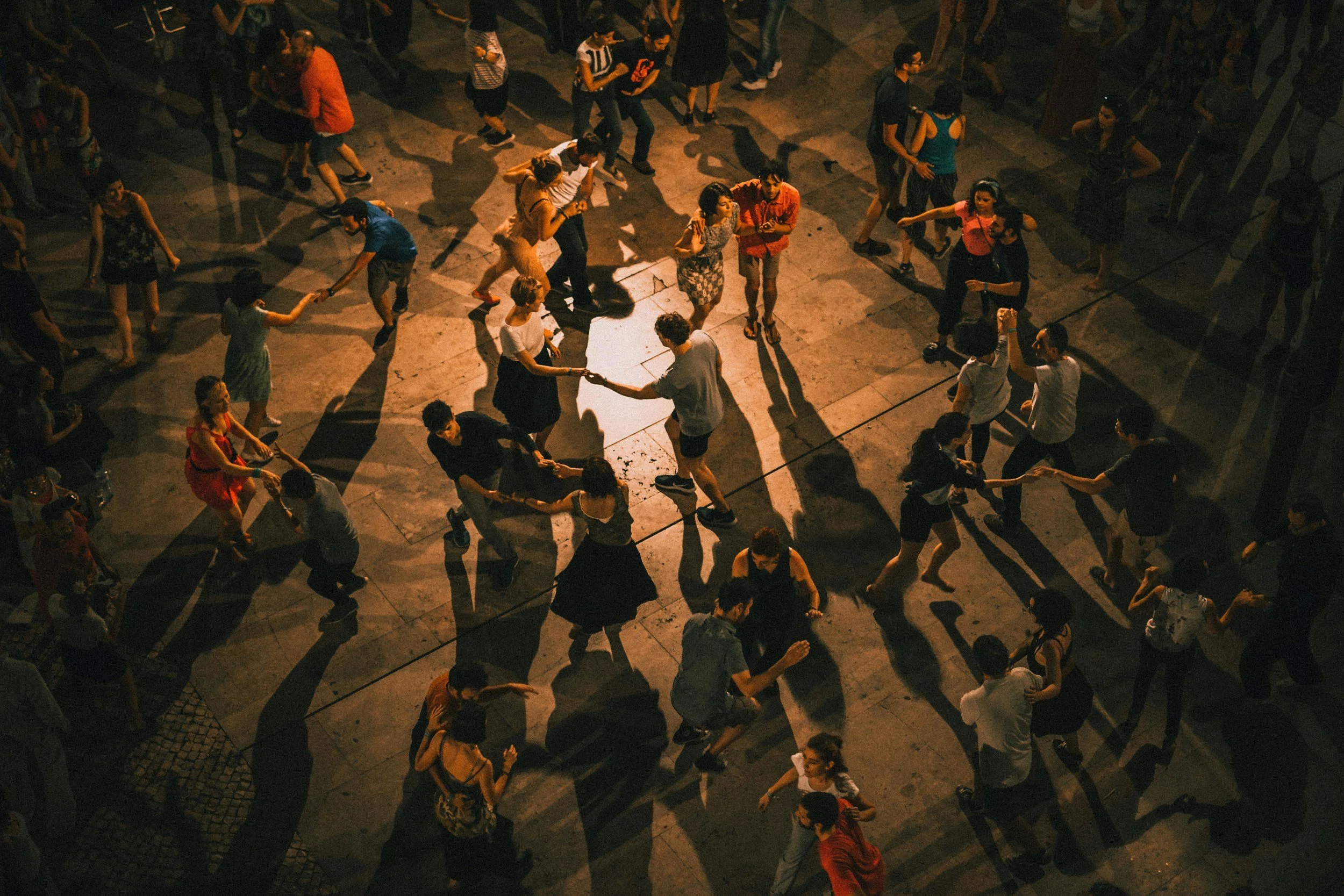 People dancing and swinging on a night-time outdoor dance floor, with shadows cast on the ground.