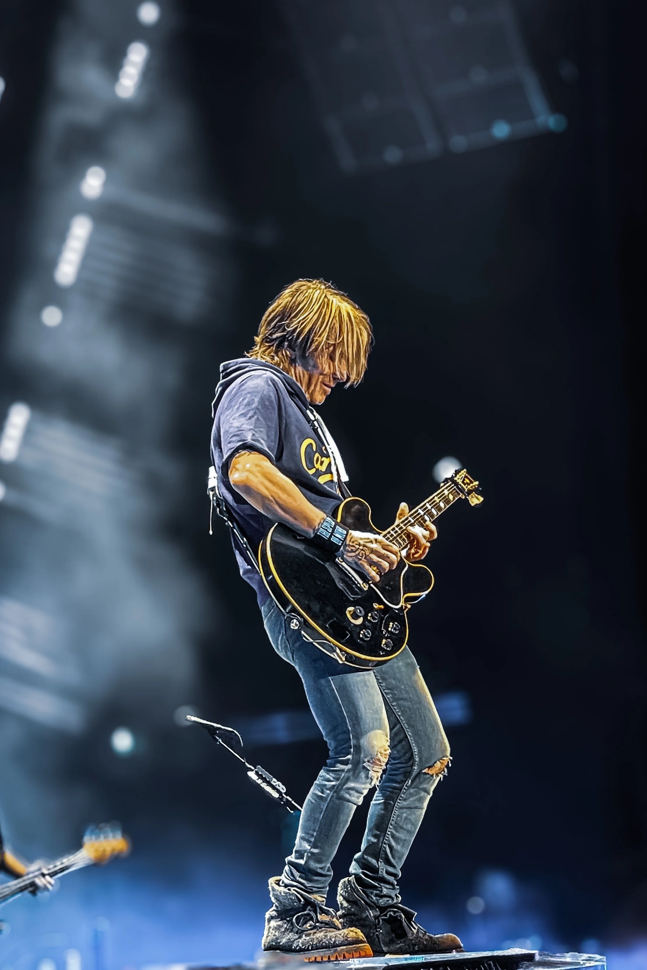 Musician playing an electric guitar on stage with stage lights and smoky atmosphere.