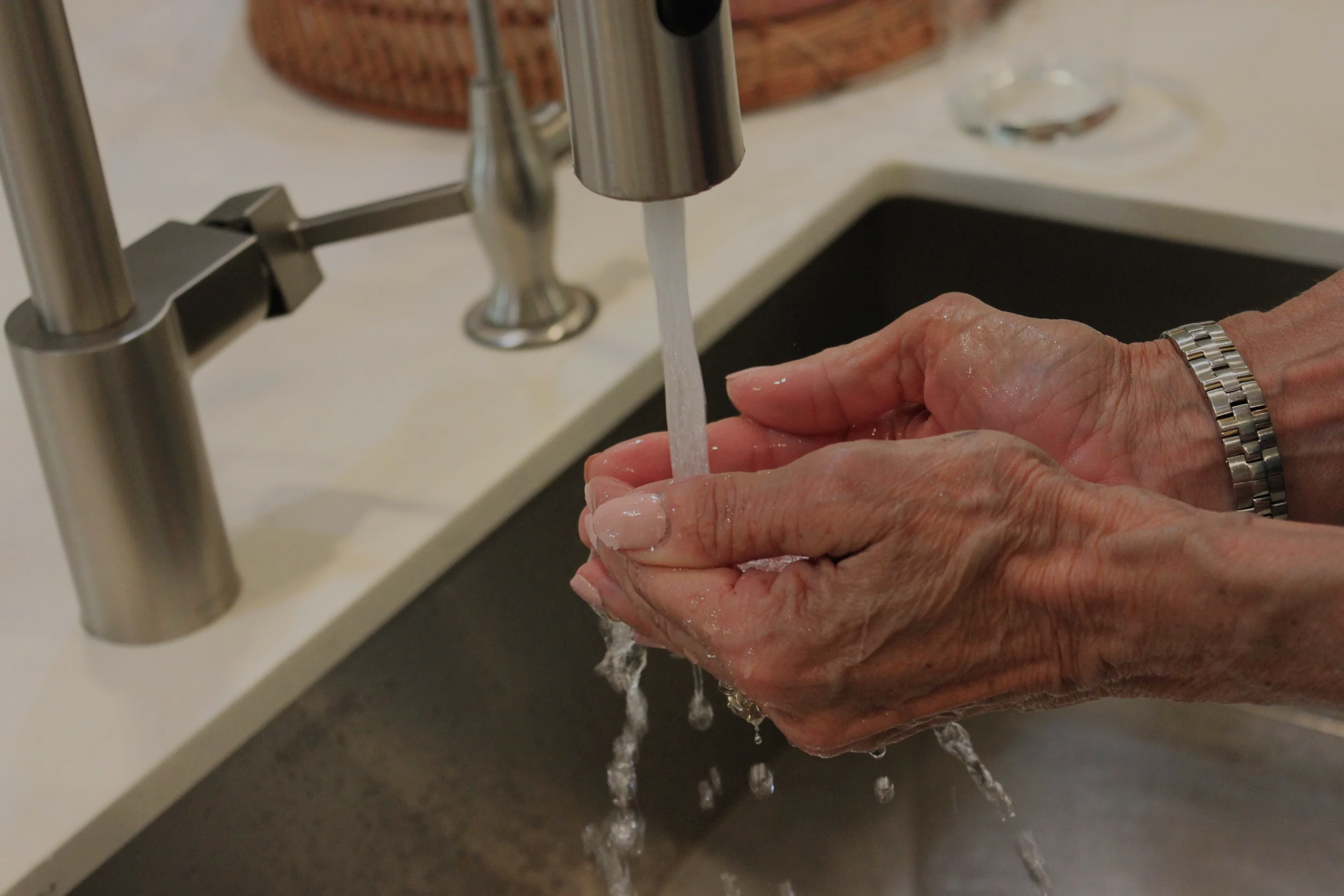 Filtered water flowing from kitchen tap with hands, representing whole house water filtration in San Diego for clean, safe drinking water