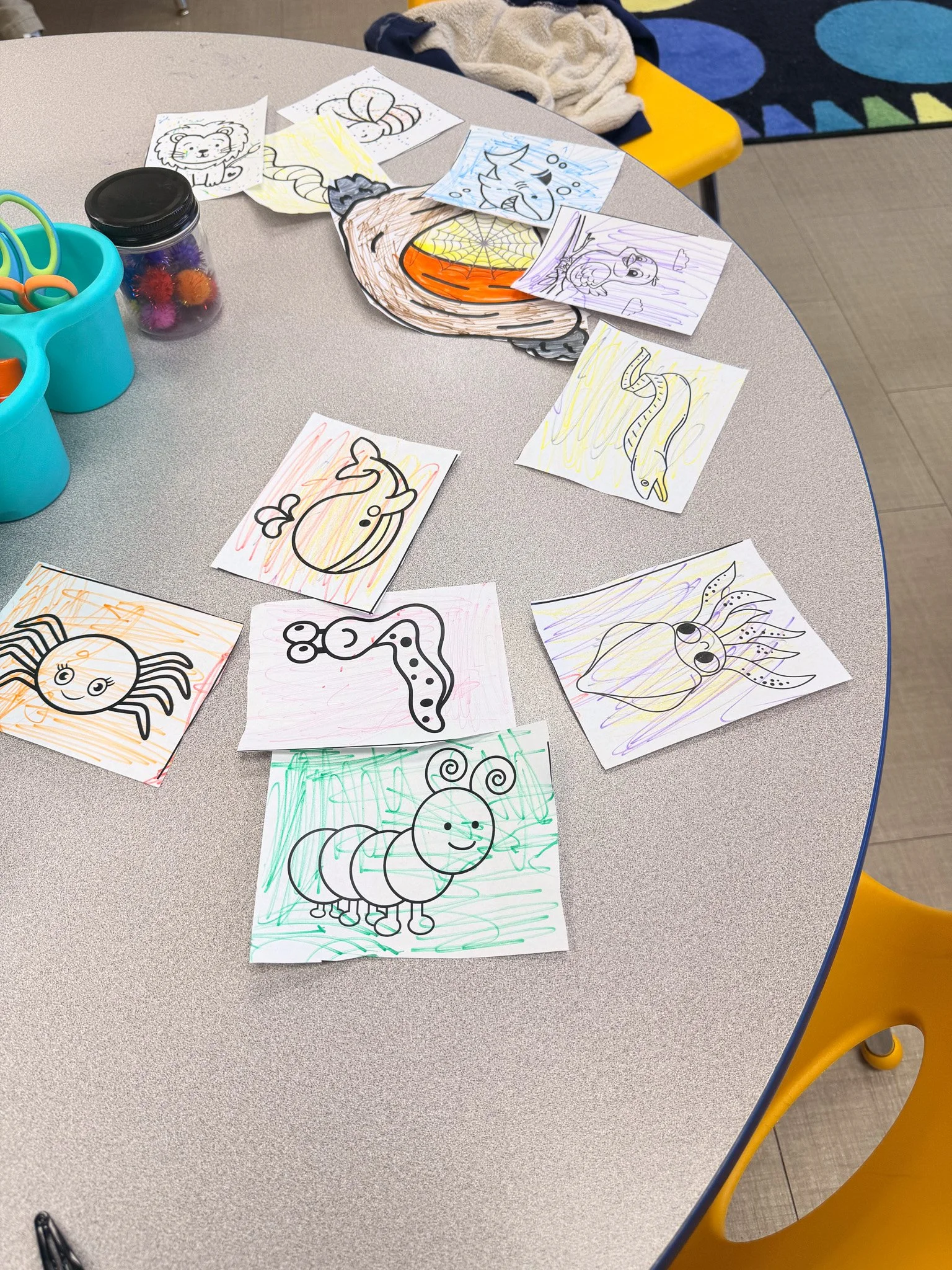 Coloring pages of various insects and animals, some partially colored, spread out on a gray table.