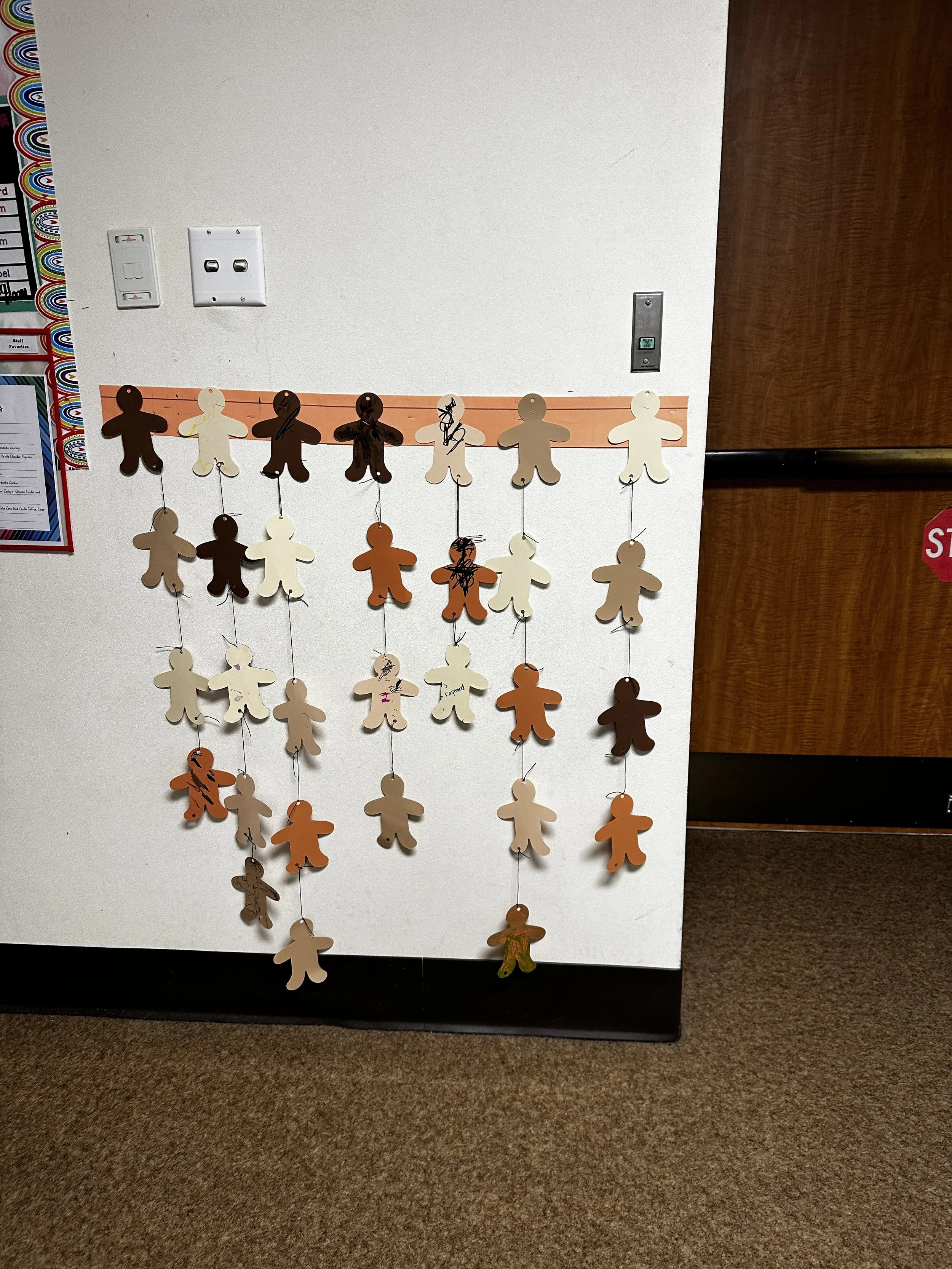 Paper gingerbread man decorations hanging on a wall in a grid pattern.