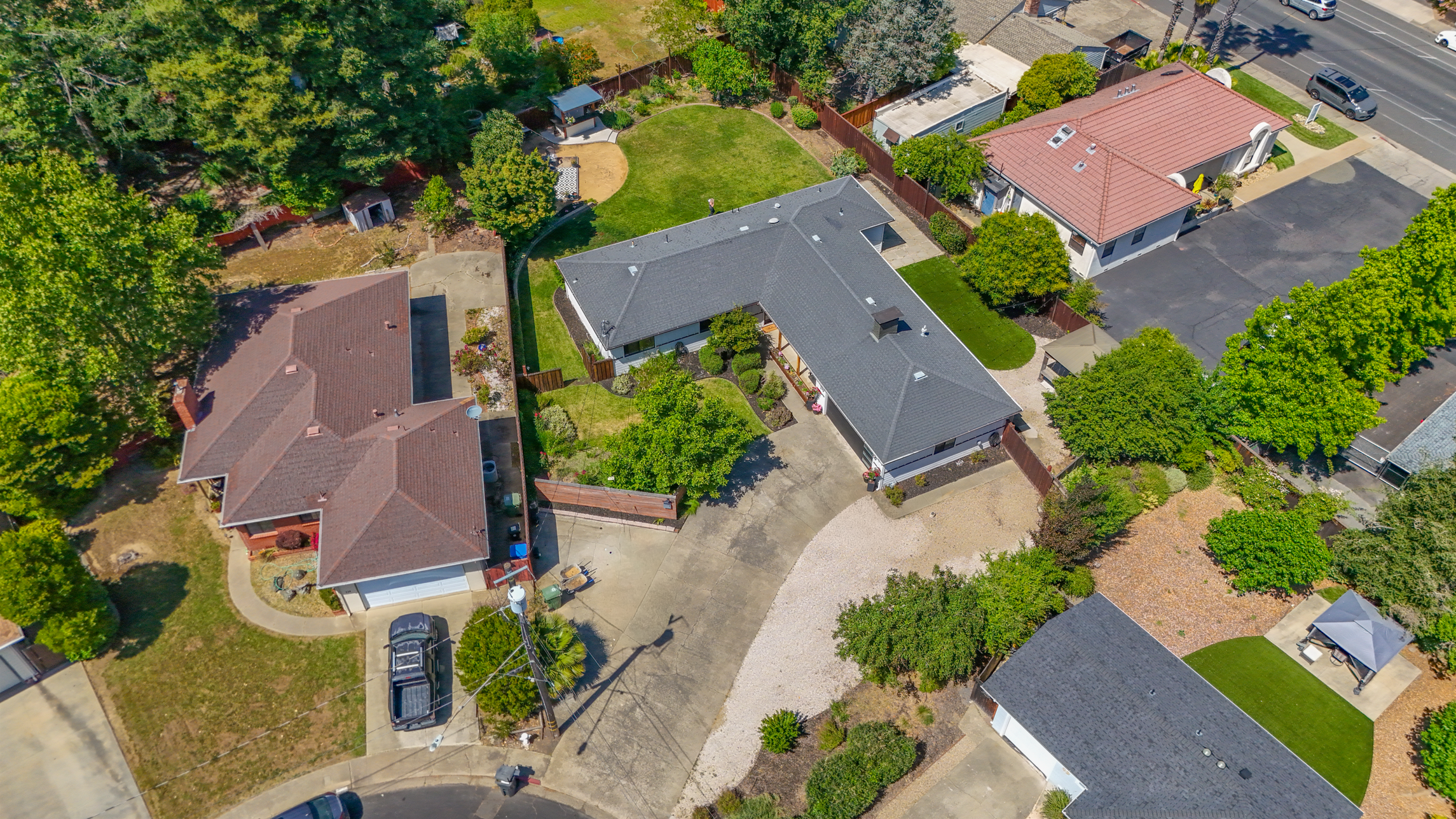 Aerial view of a neighborhood showing several houses, trees, a lawn, a driveway, and parked cars.