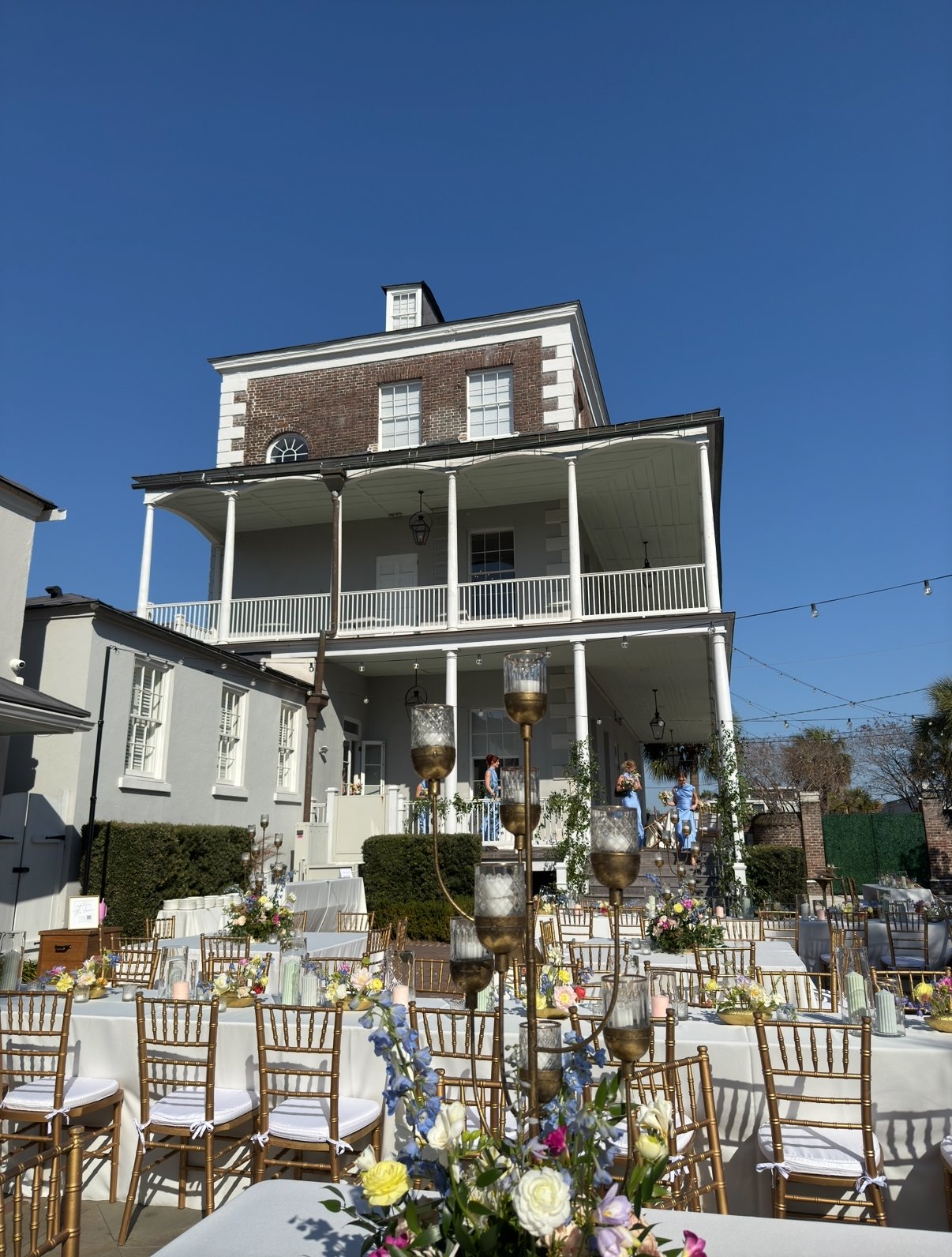 Outdoor wedding venue with decorated tables and chairs in front of a historic building under a clear blue sky.