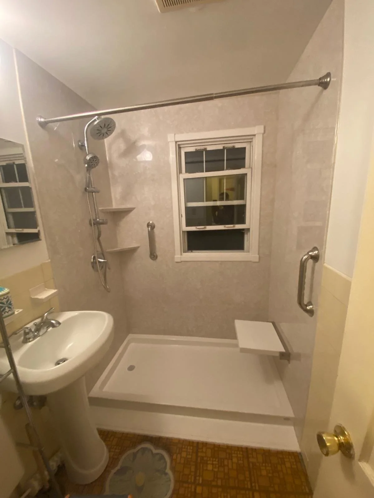 Bathroom with a walk-in shower, a small window, a white sink, and a patterned brown floor.